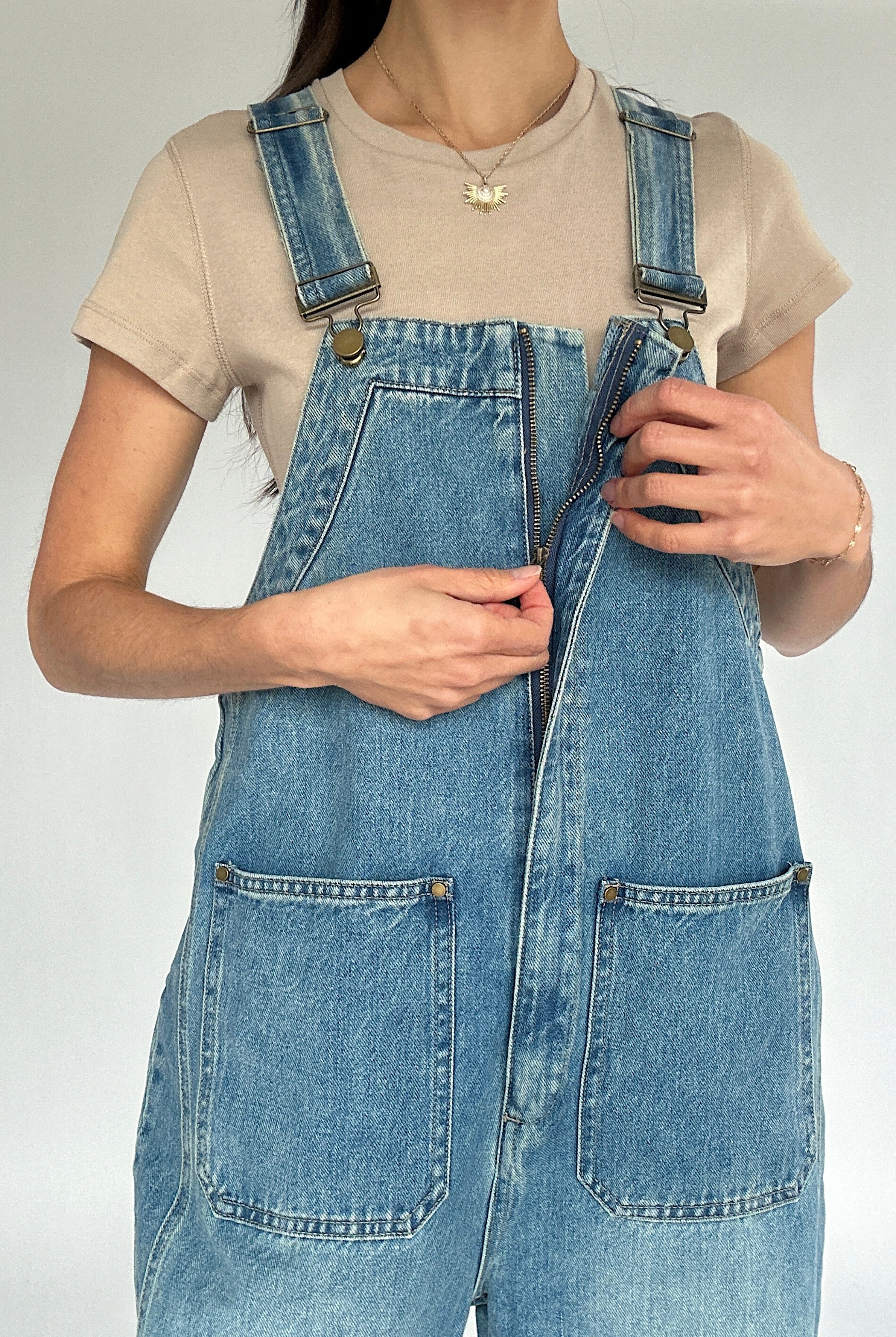 Person wearing a denim overalls with a plain background showing front zipper detail