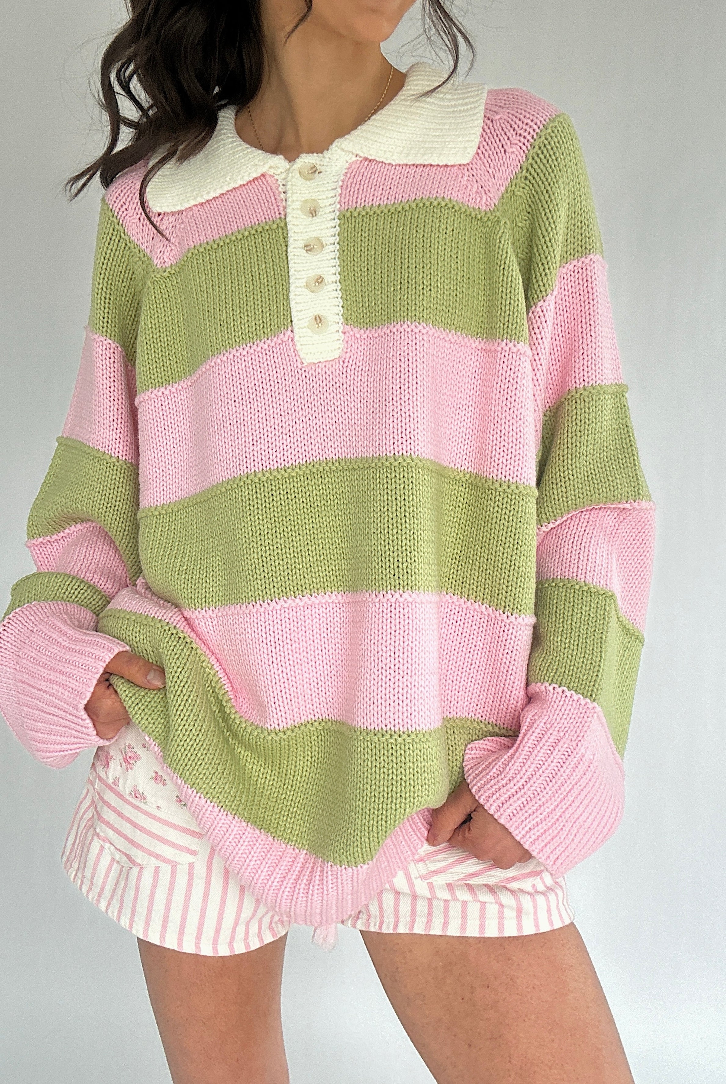 Person wearing a green and pink striped sweater with a plain background