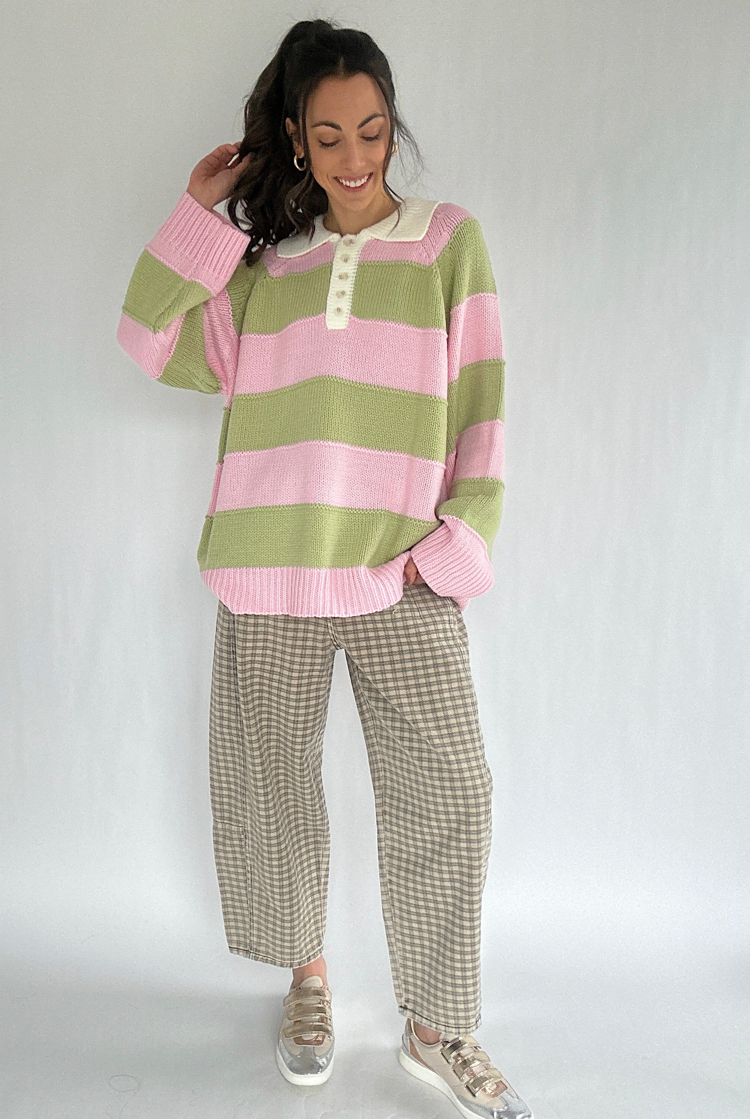 Woman wearing a pink and green striped sweater with checkered pants on a white background