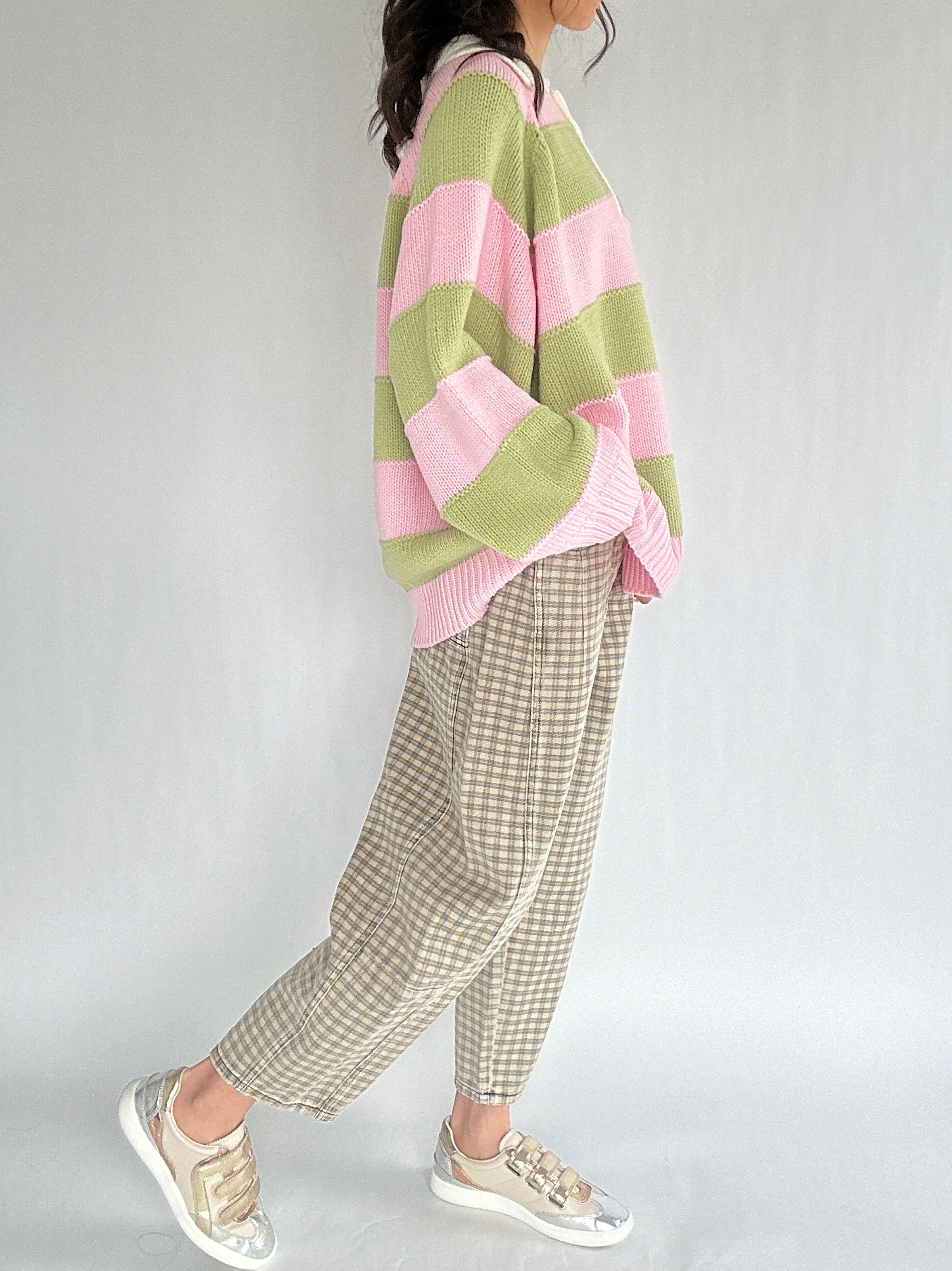 Person wearing a pink and green striped sweater with plaid pants on a plain background from side