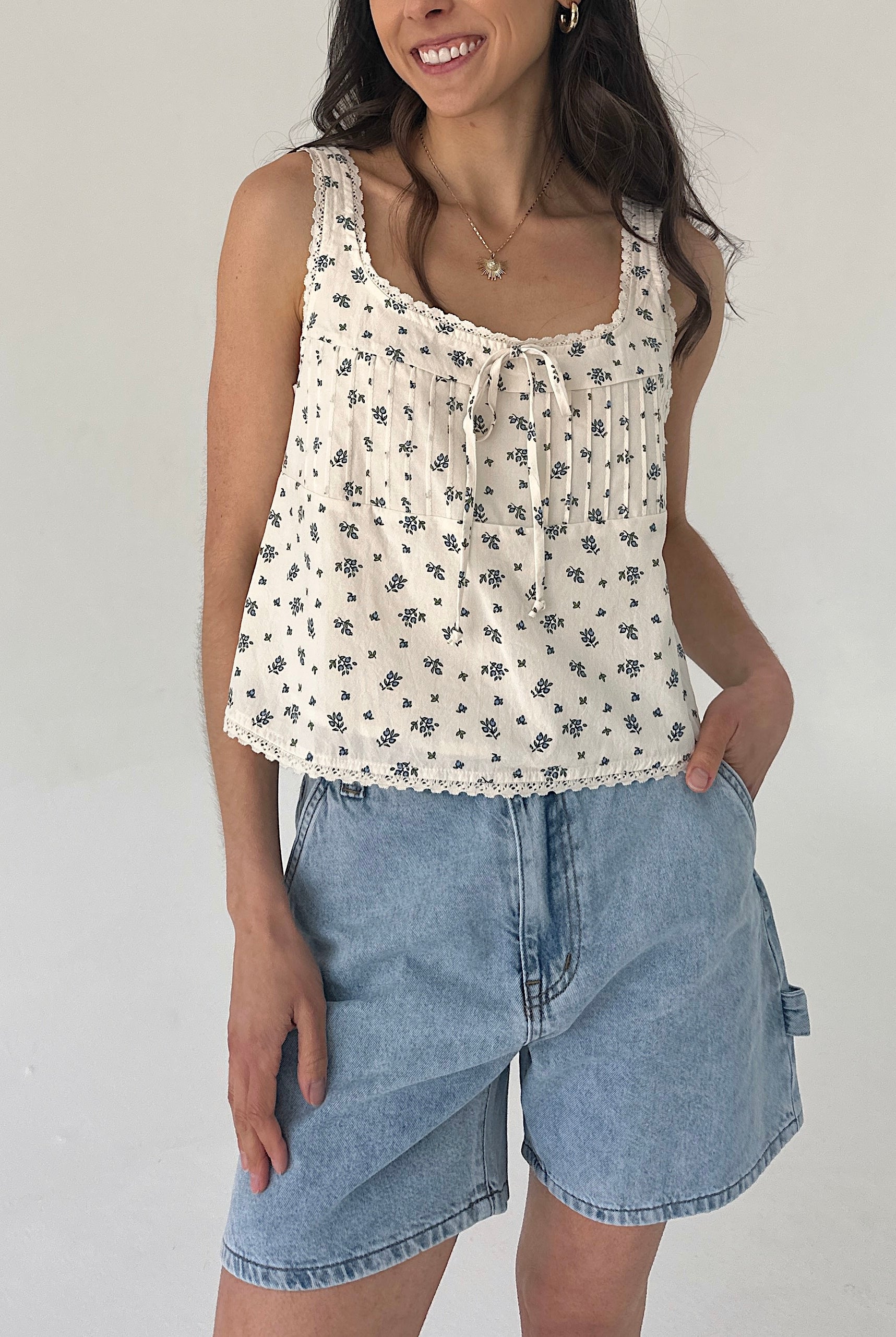 Woman wearing a floral sleeveless top and denim shorts against a plain background