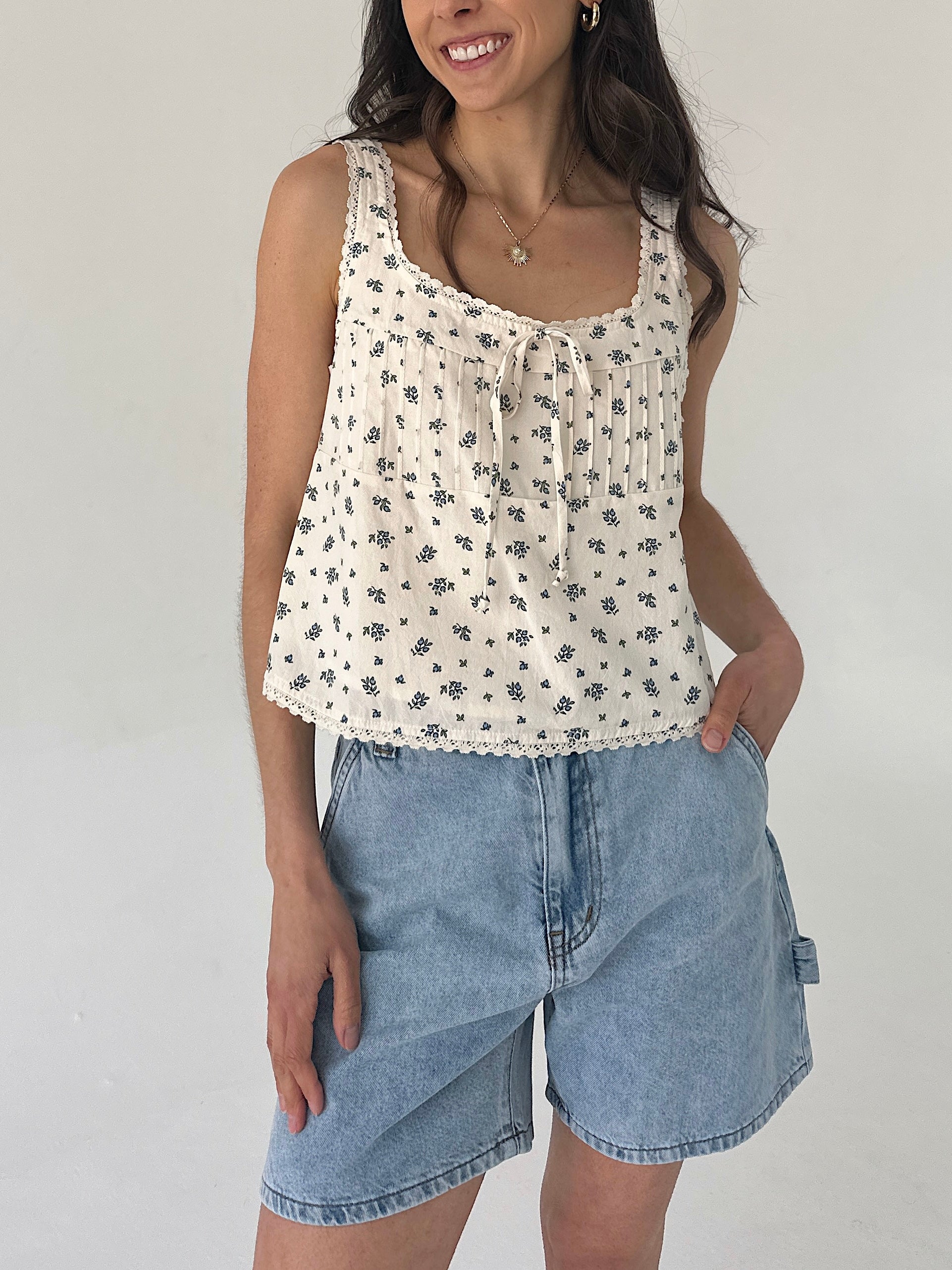 Woman wearing a floral sleeveless top and denim shorts against a plain background