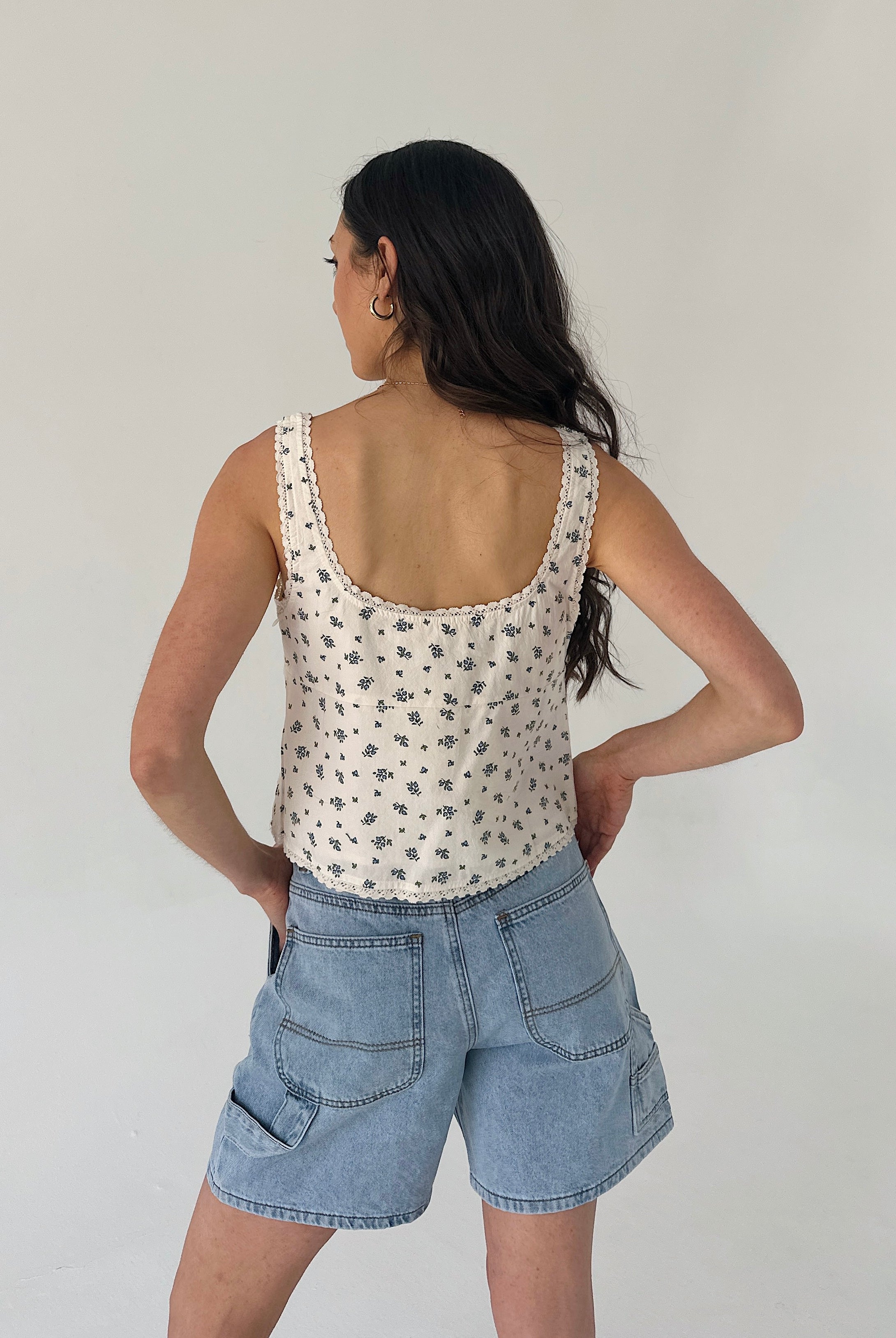 Woman wearing a patterned tank top and denim shorts against a plain background