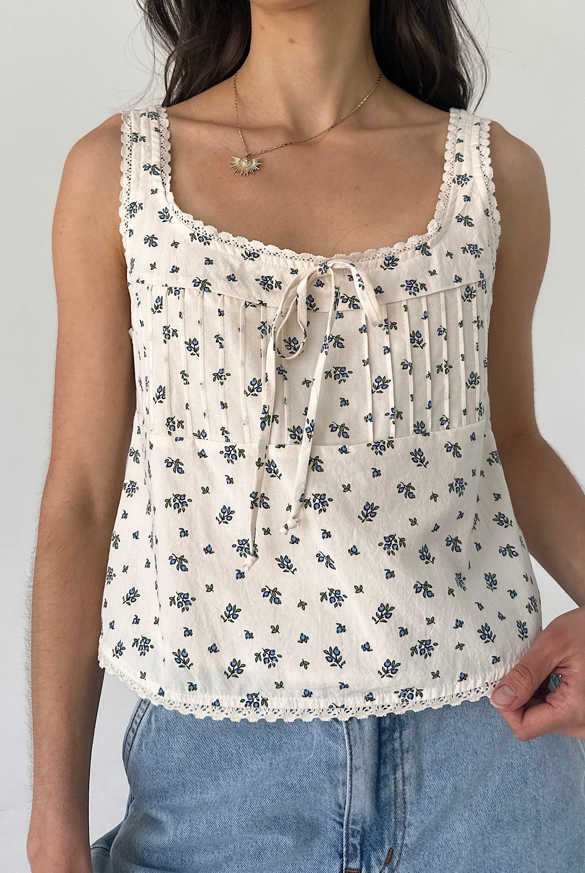 Woman wearing a white floral tank top against a plain background