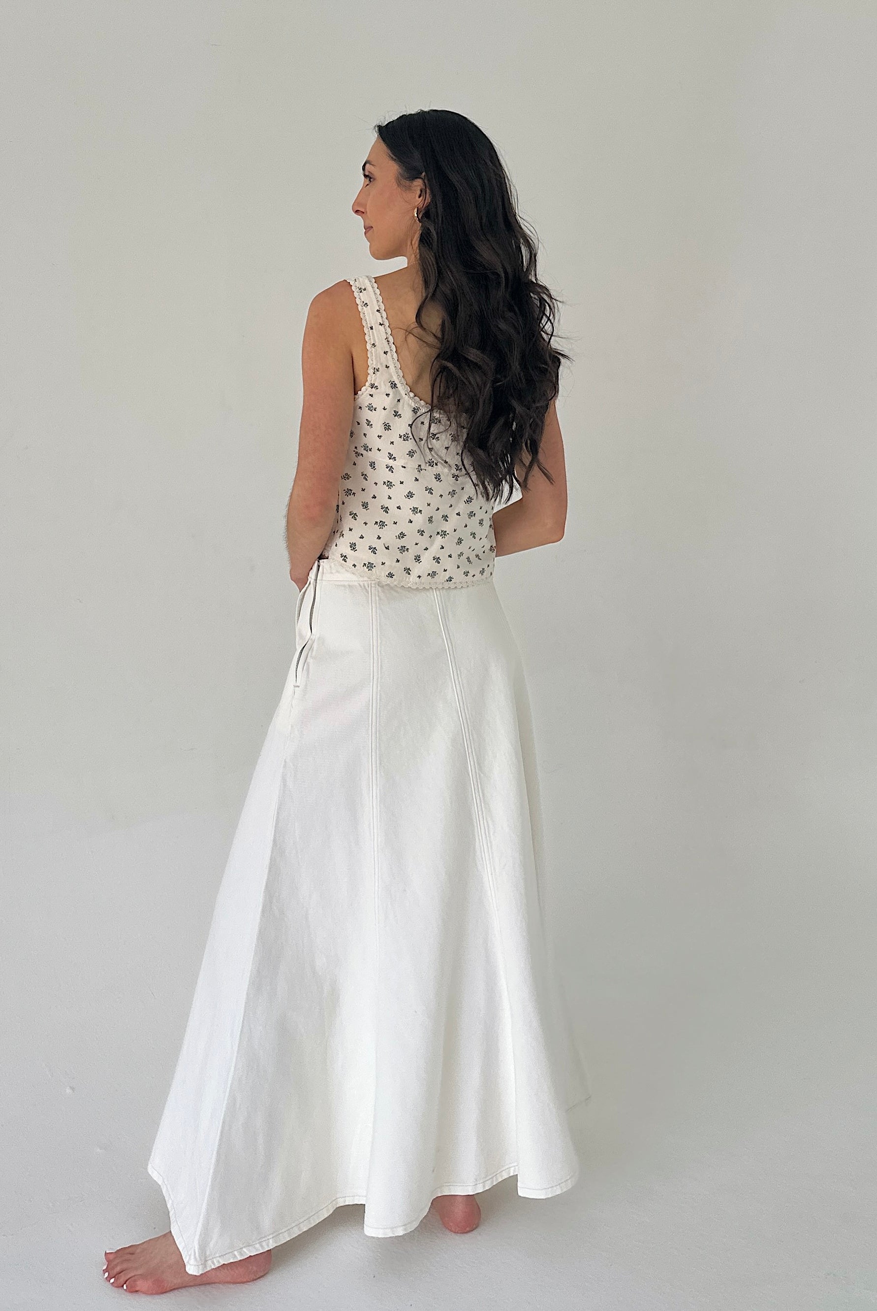 Woman wearing a floral top and white skirt on a plain background showing back