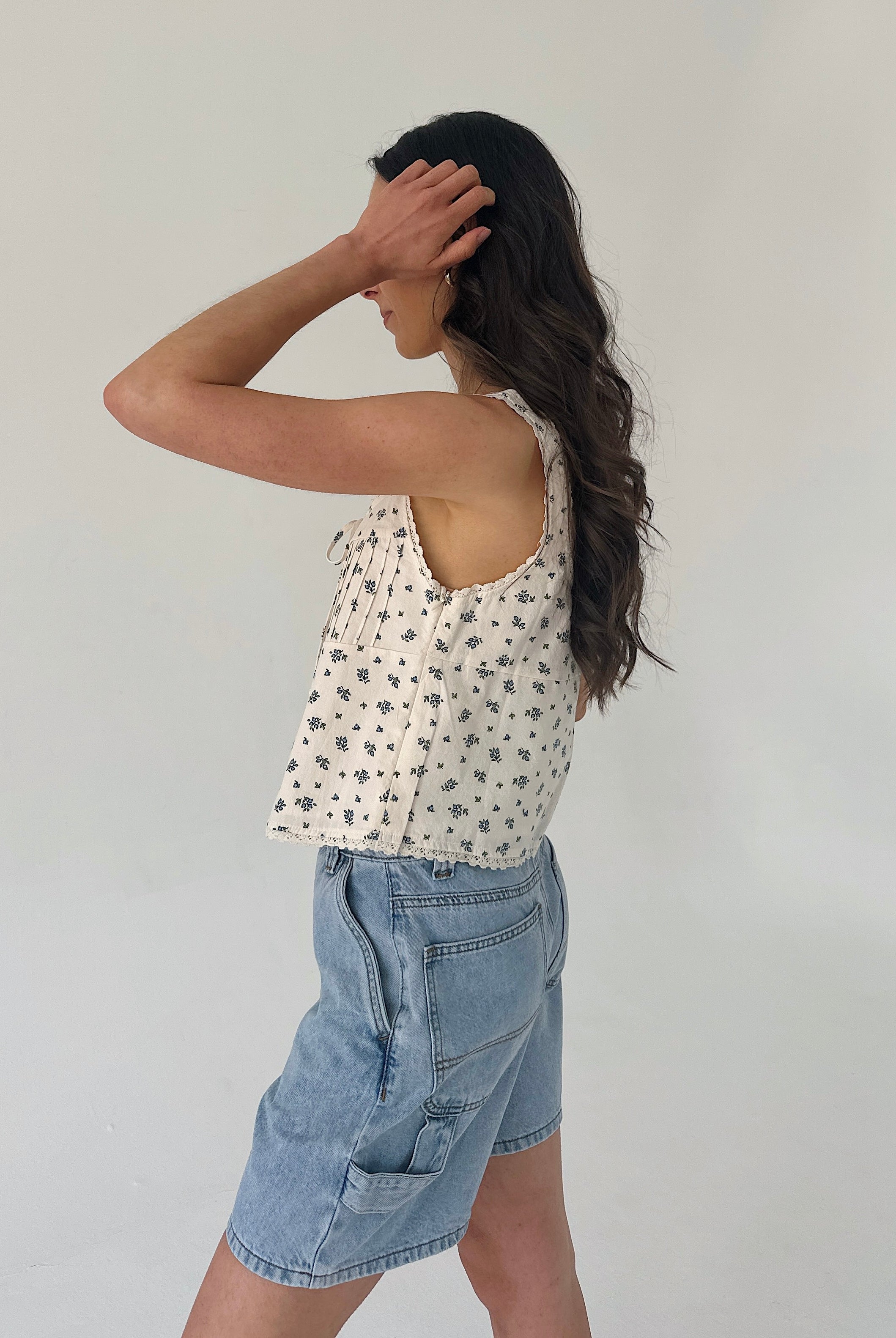 Woman wearing a patterned top and denim shorts against a plain background