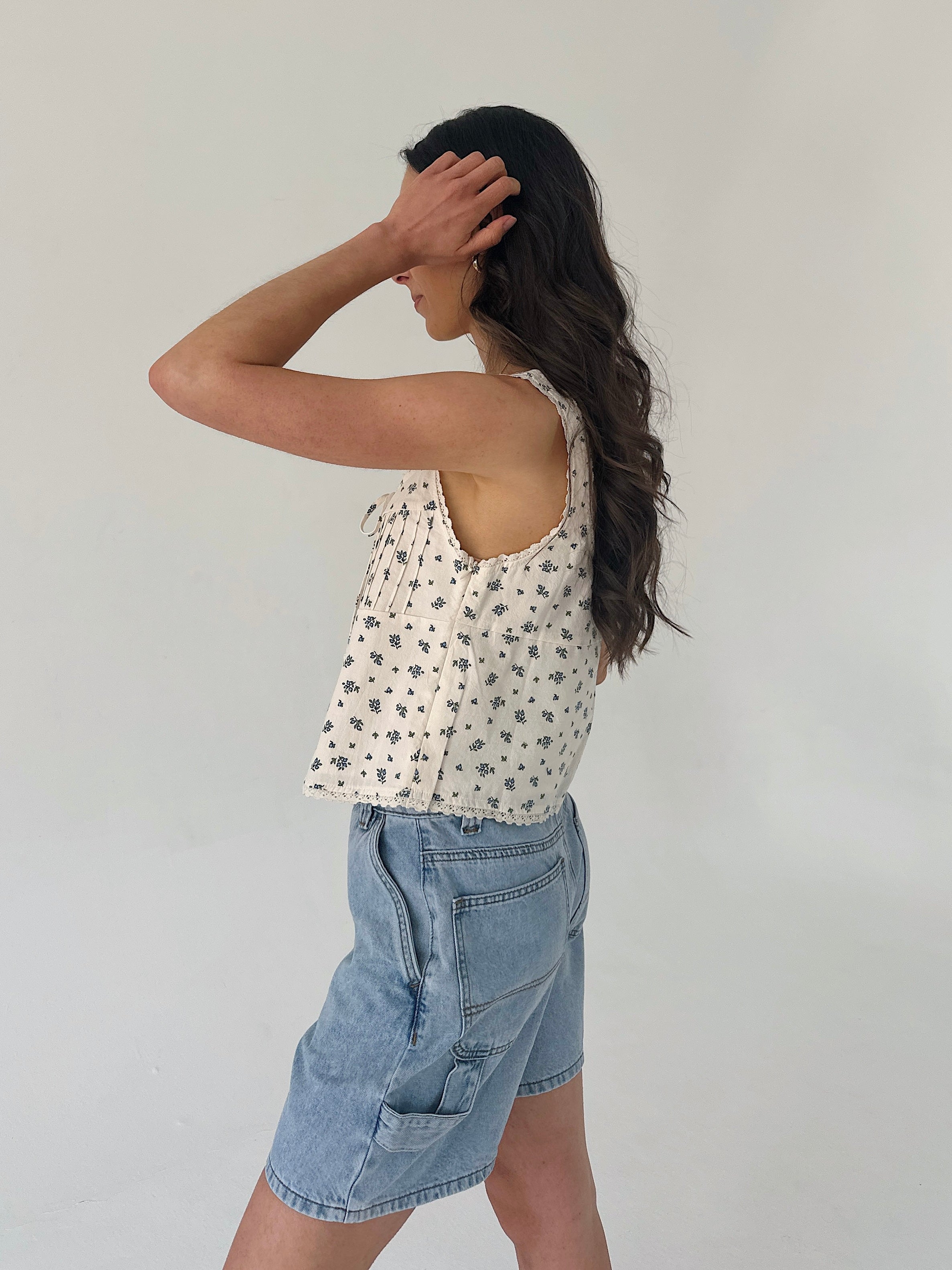 Woman wearing a patterned top and denim shorts against a plain background