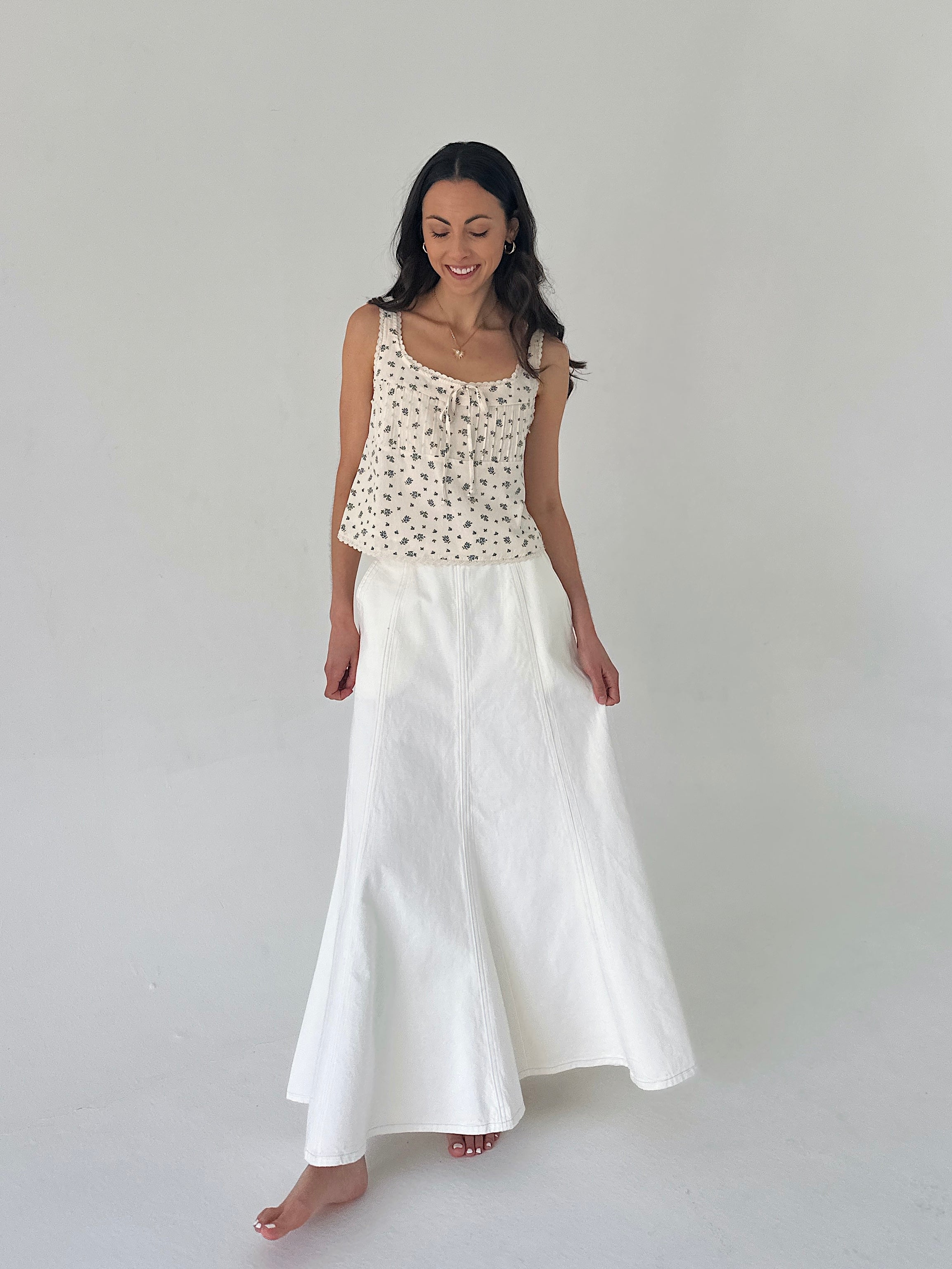 Woman wearing a floral top and white skirt on a plain background