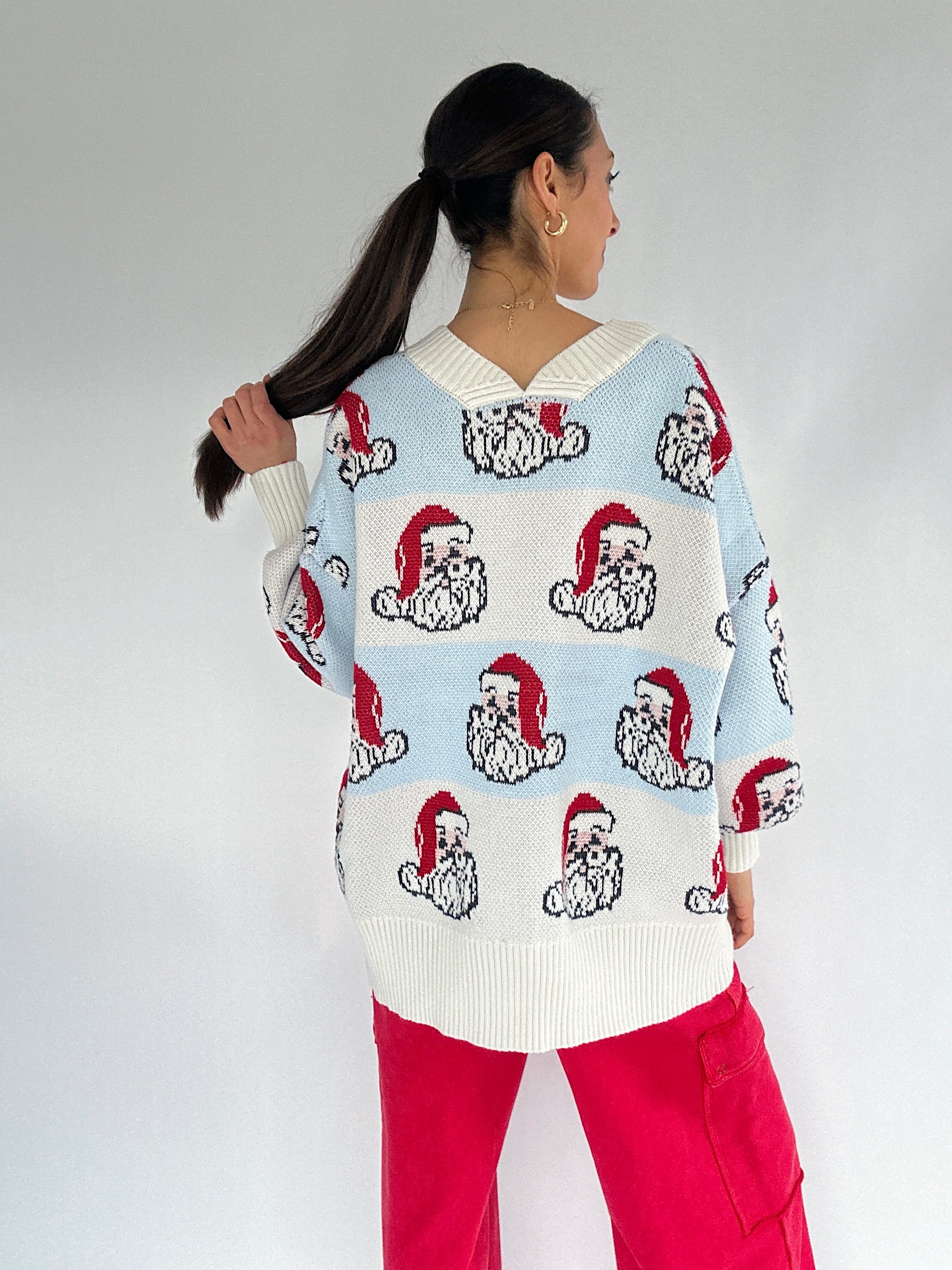 Person wearing a sweater with Santa Claus faces pattern on a plain background