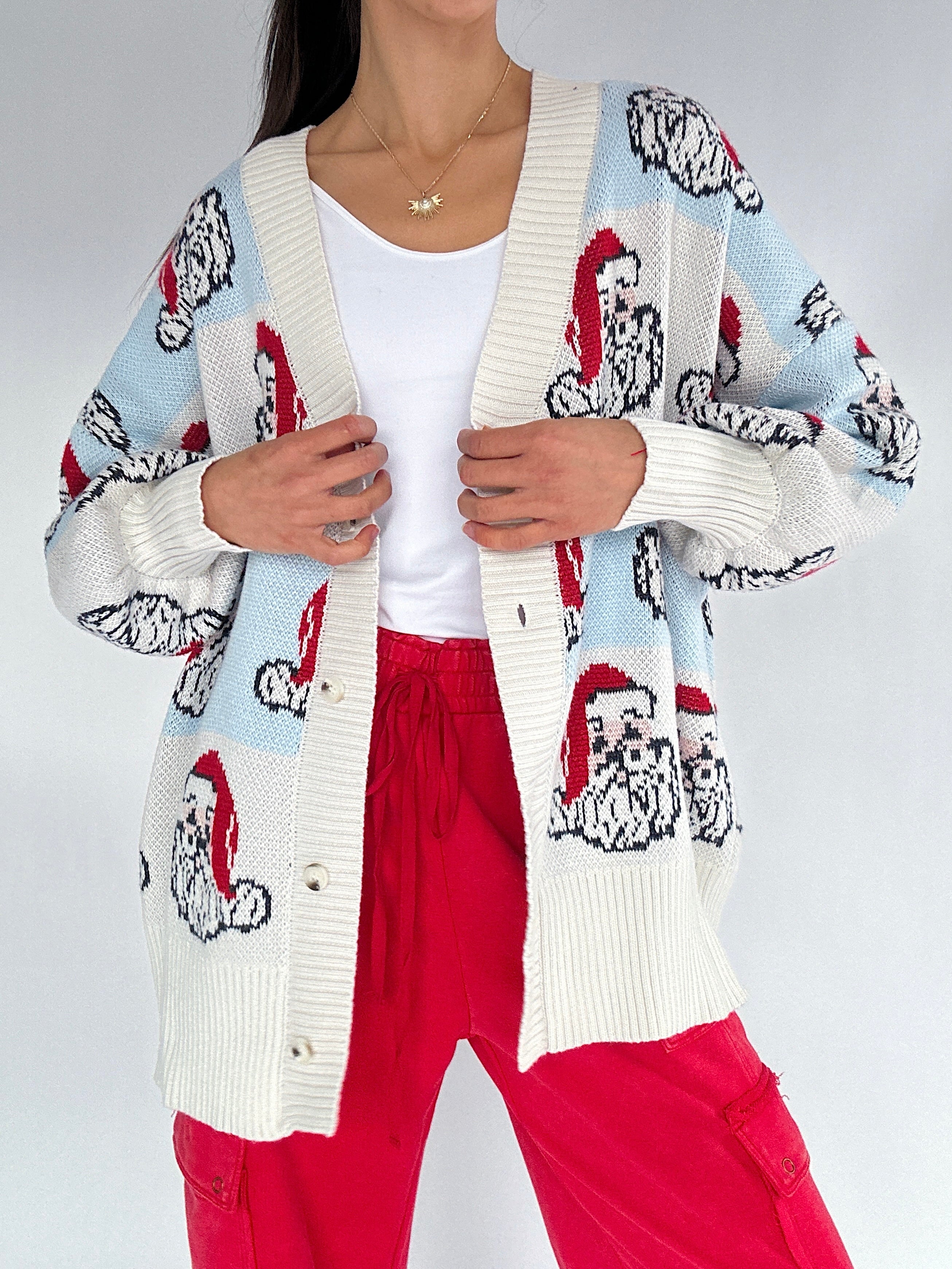 Person wearing a patterned cardigan with cartoon Santa faces on a plain background