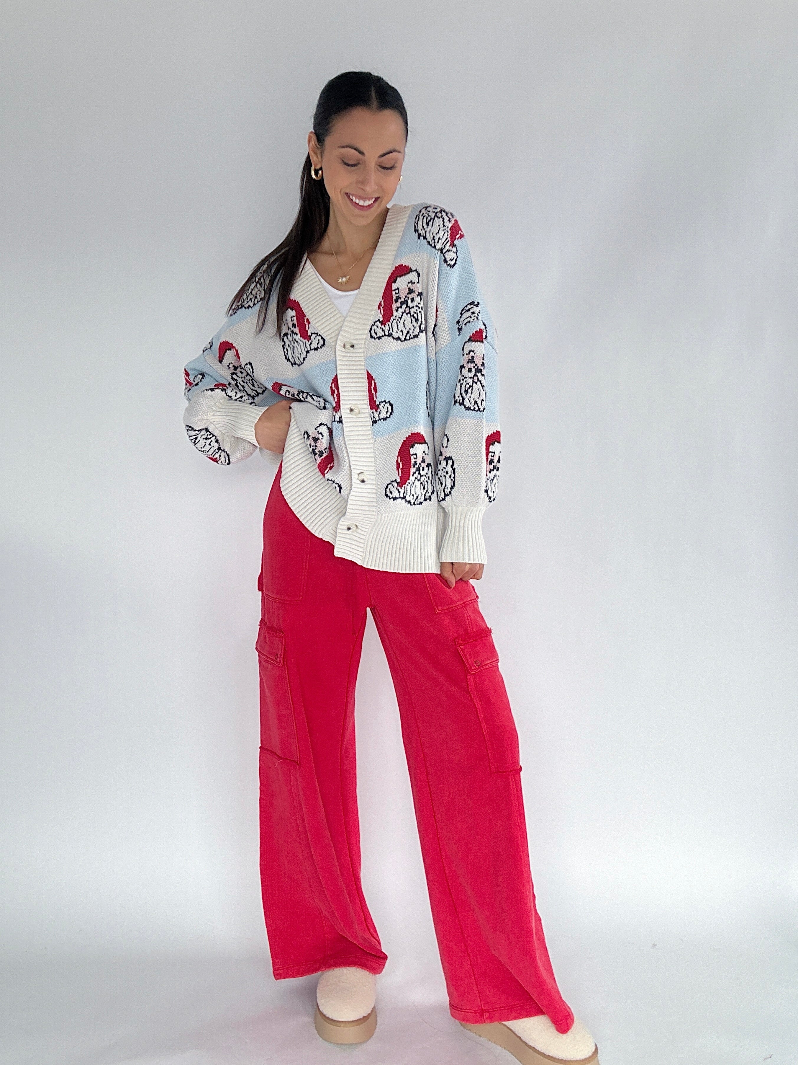 Woman wearing a Santa face patterned cardigan and red pants on a white background