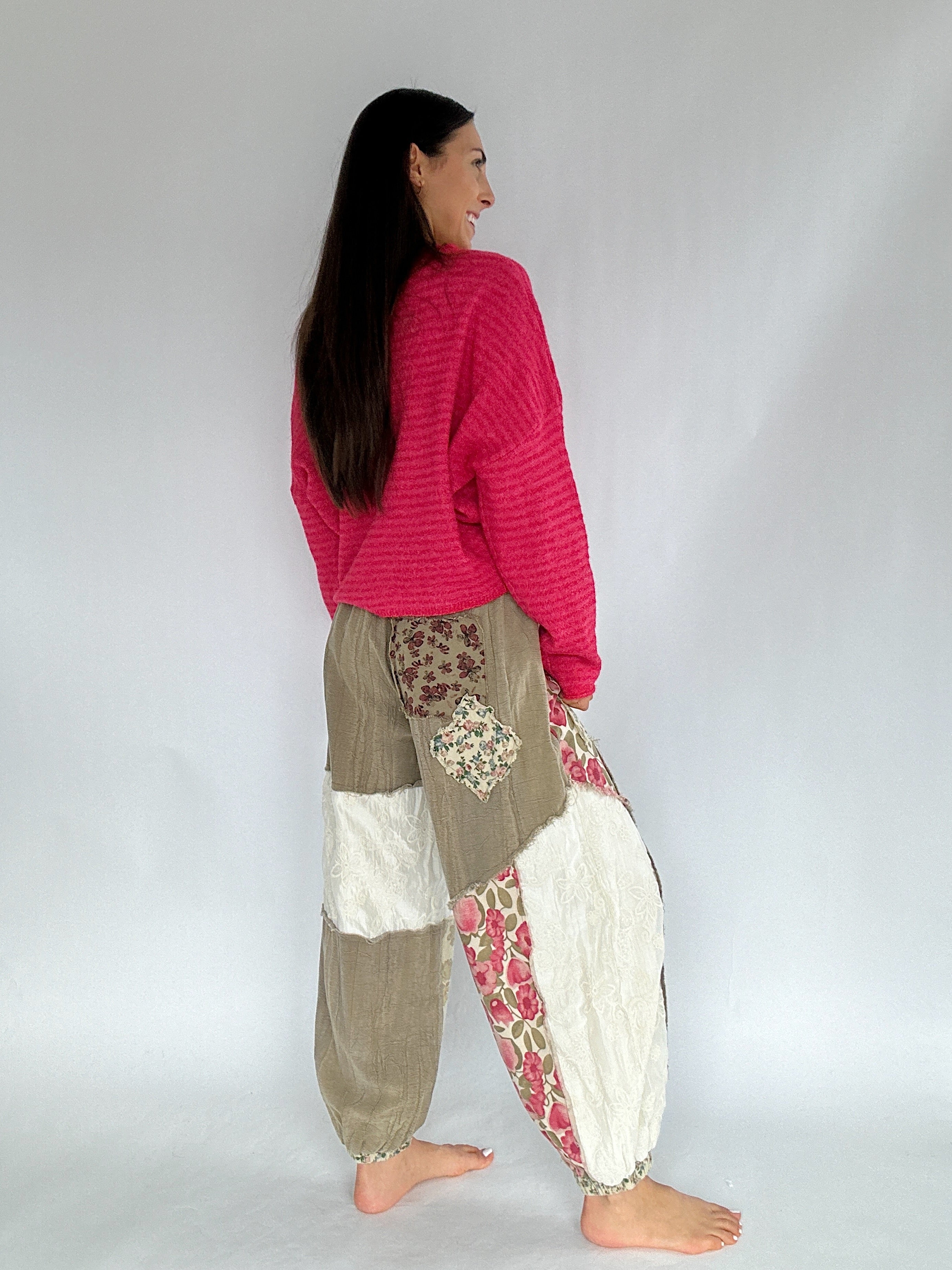 Woman wearing a pink sweater and patchwork pants against a plain background