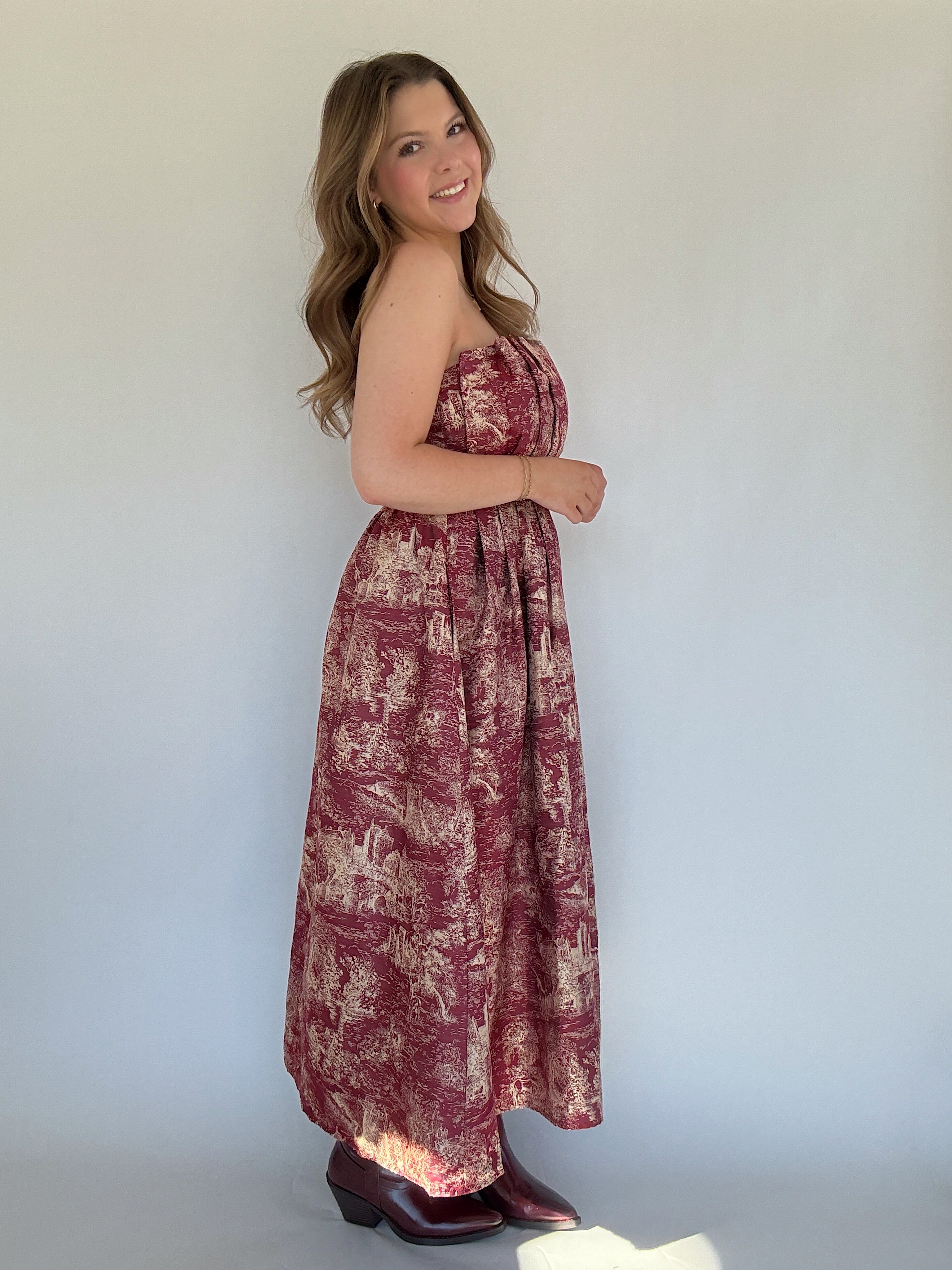 Woman wearing a floral strapless dress against a plain background from side
