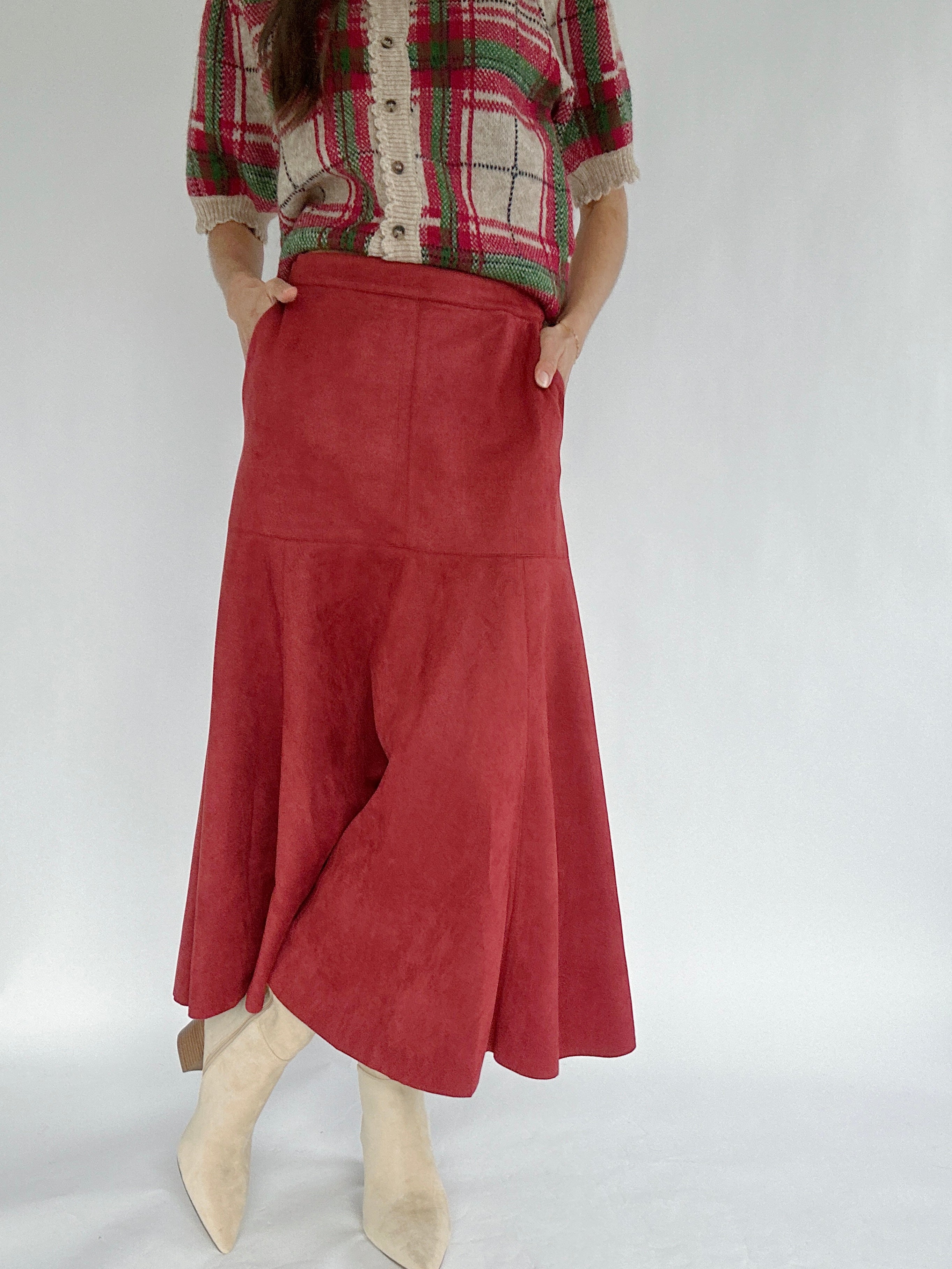 Person wearing a red plaid sweater and red suede skirt on a white background