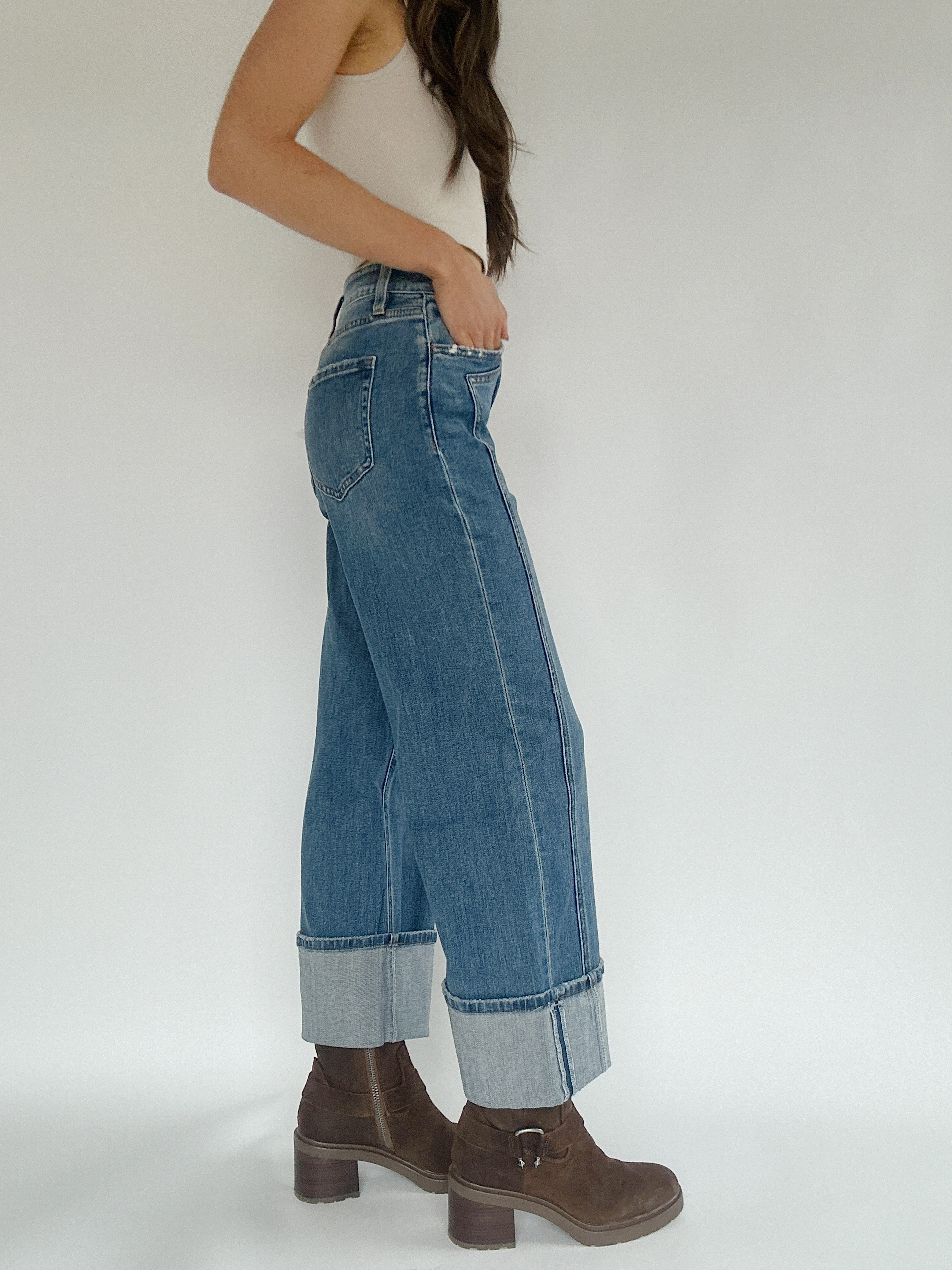 Woman wearing medium wash wide leg jeans ith a cuffed bottom showing the side.