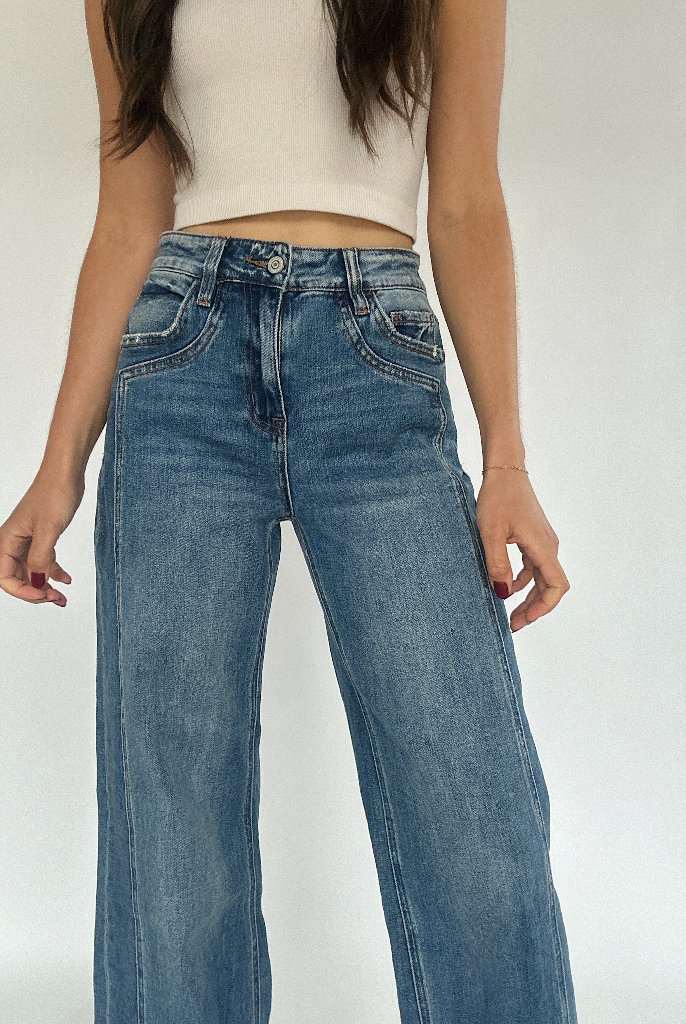 Woman wearing medium washed denim jeans with zip fly, button and pockets.