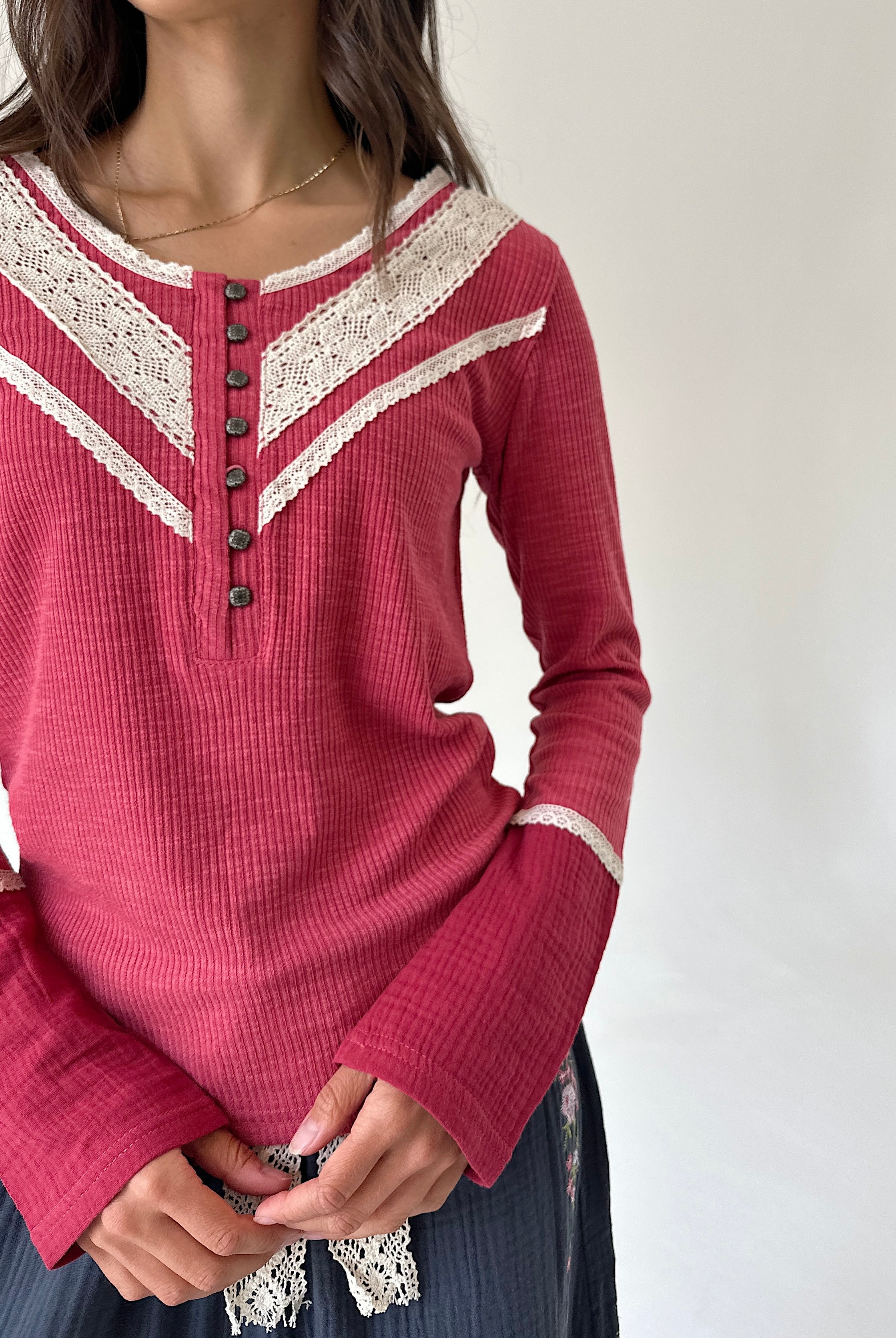 A woman wearing a long-sleeve knit henley top in dusty rose pink with cream lace trim and dark buttons, paired with a dark skirt.