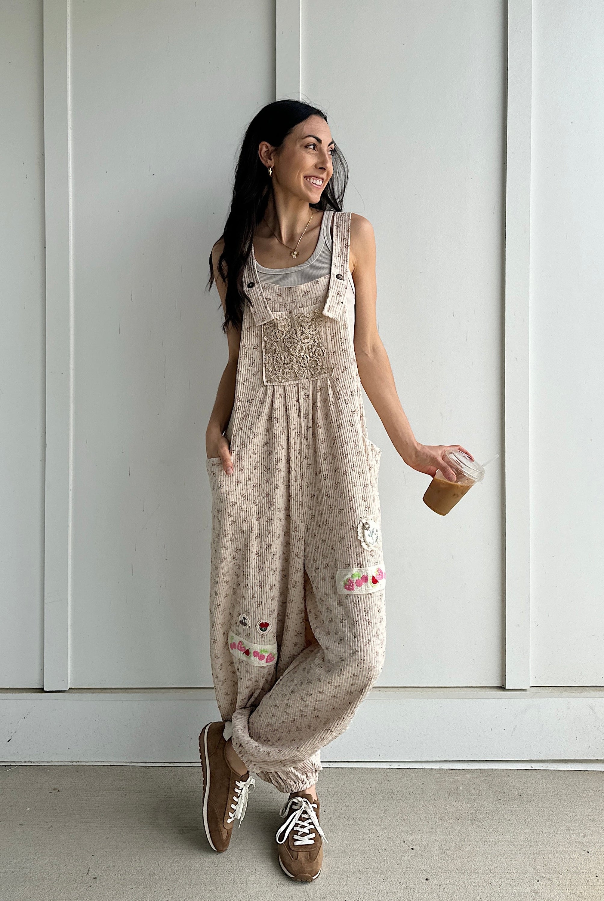 Woman wearing a patterned overalls standing against a white paneled wall.