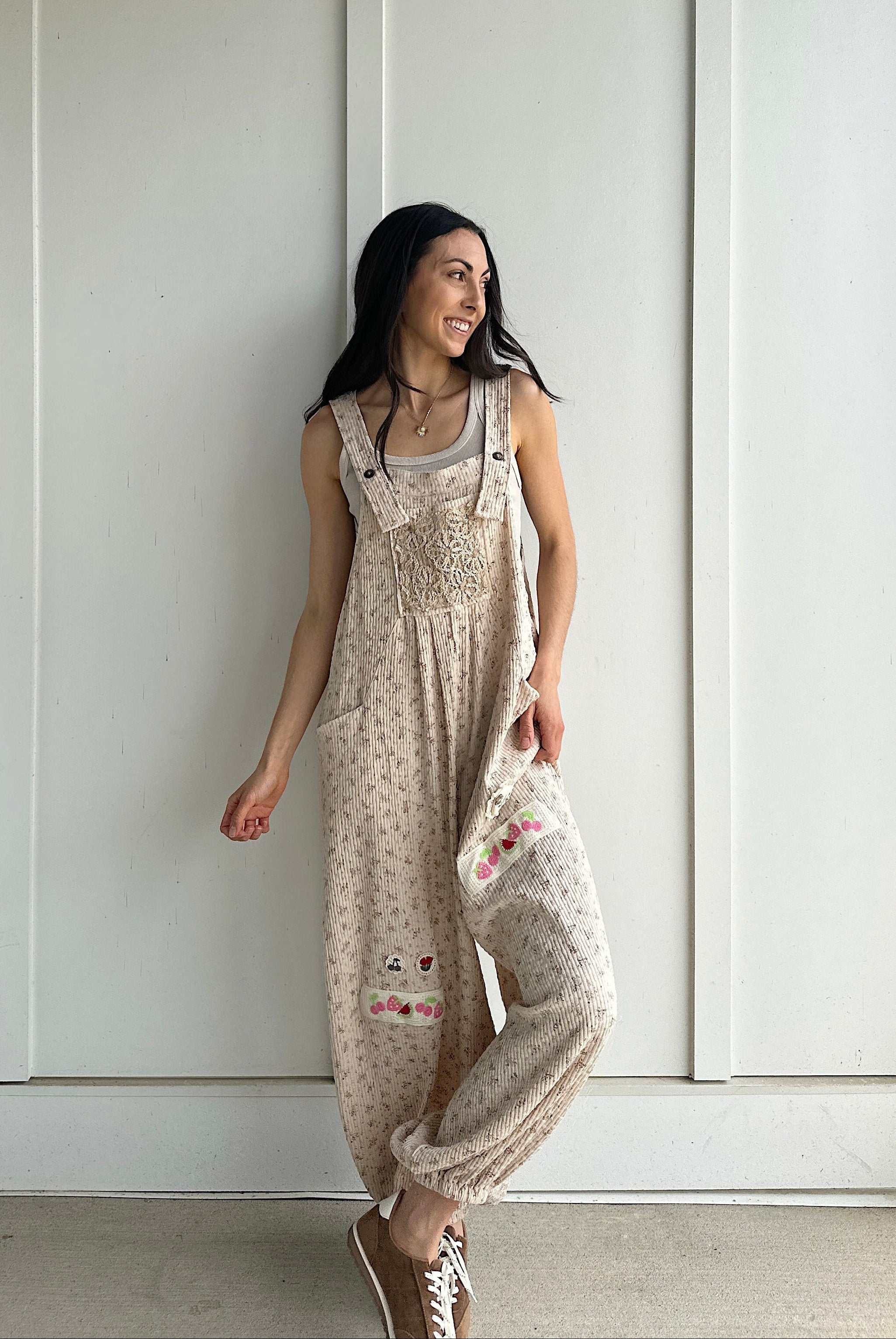Woman wearing a patterned overalls standing against a white paneled wall.