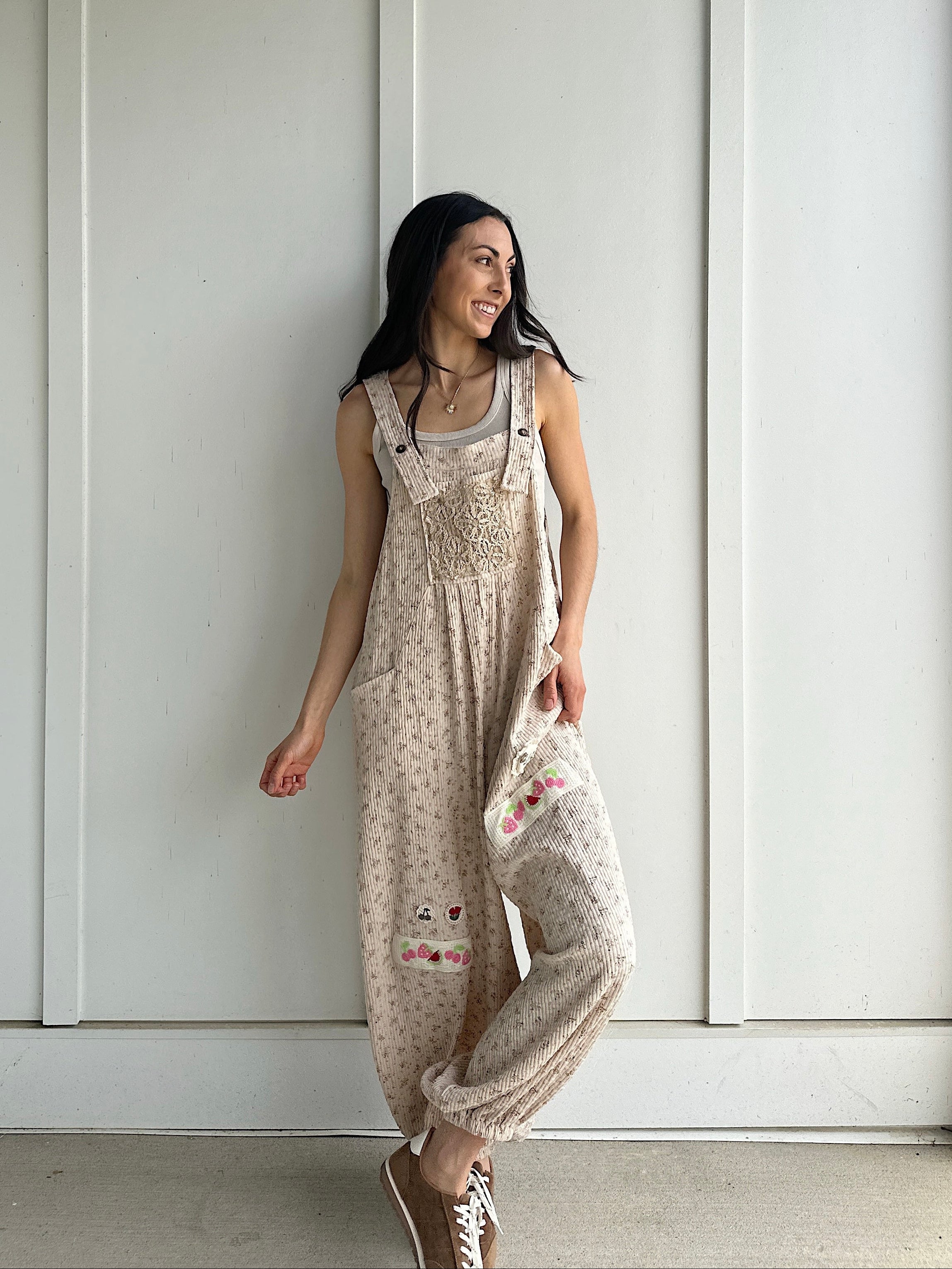 Woman wearing a patterned overalls standing against a white paneled wall.