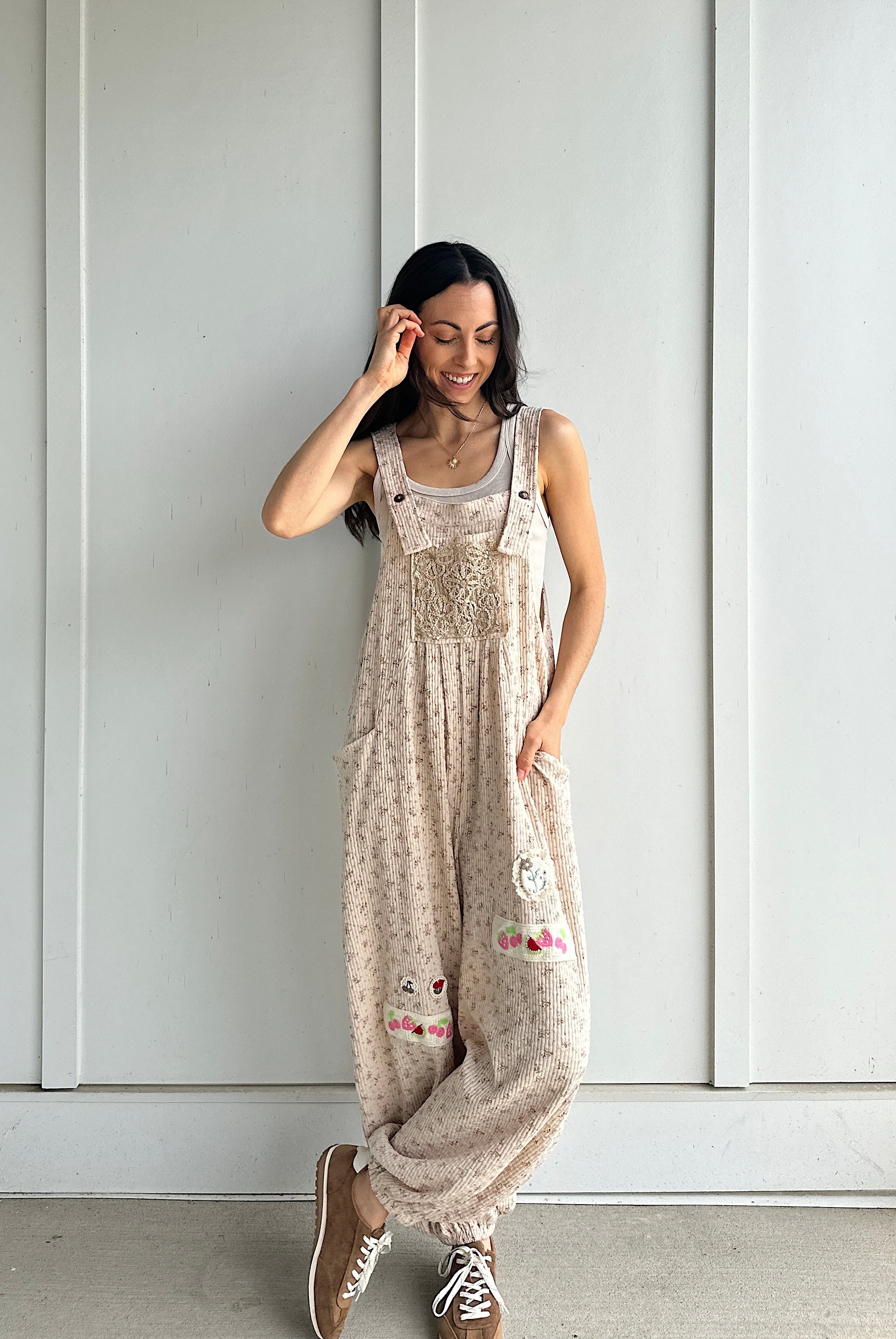 Woman wearing a patterned overalls standing against a white paneled wall.