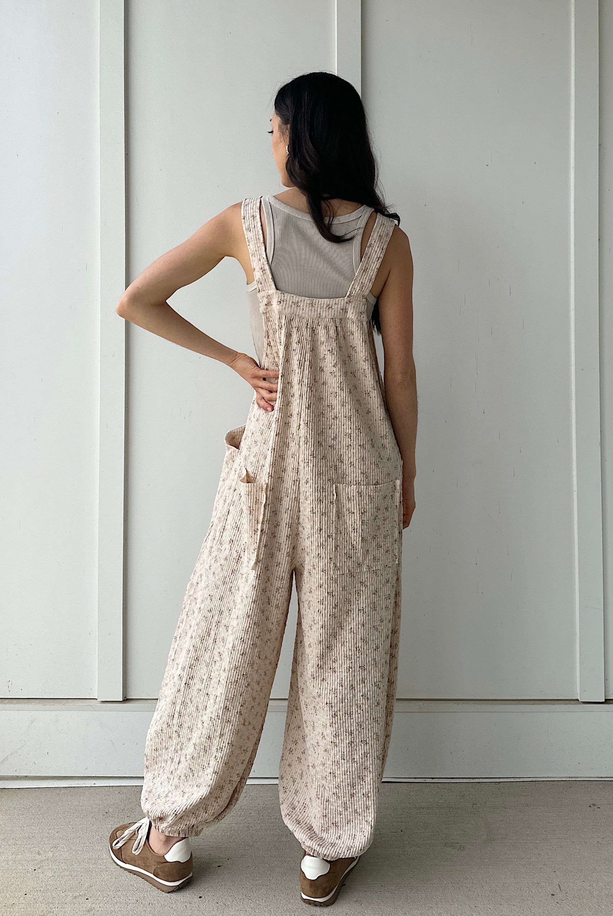 Woman wearing a floral overalls against a white wall showing the back