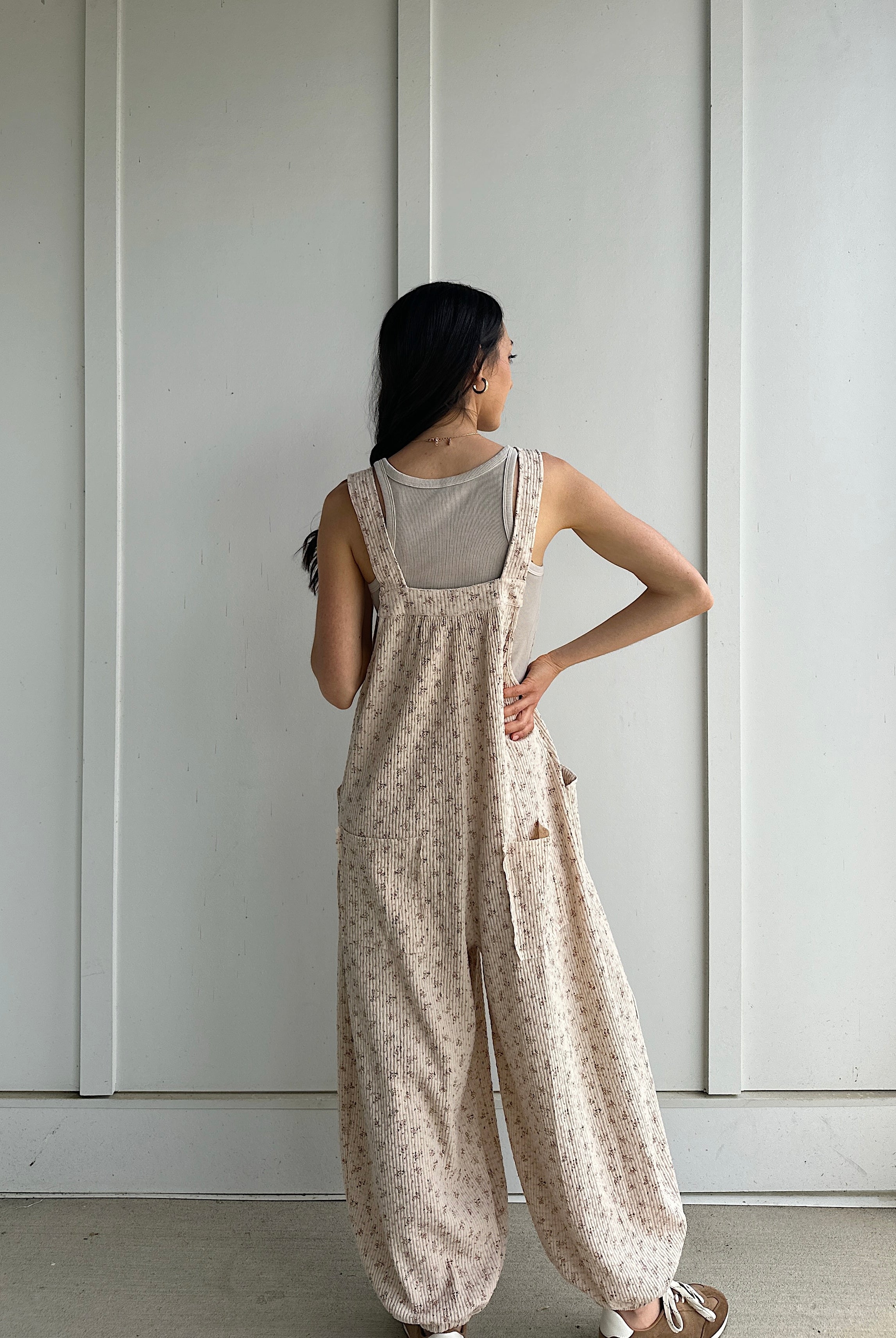 Woman wearing a floral jumpsuit standing against a plain white wall showing the back