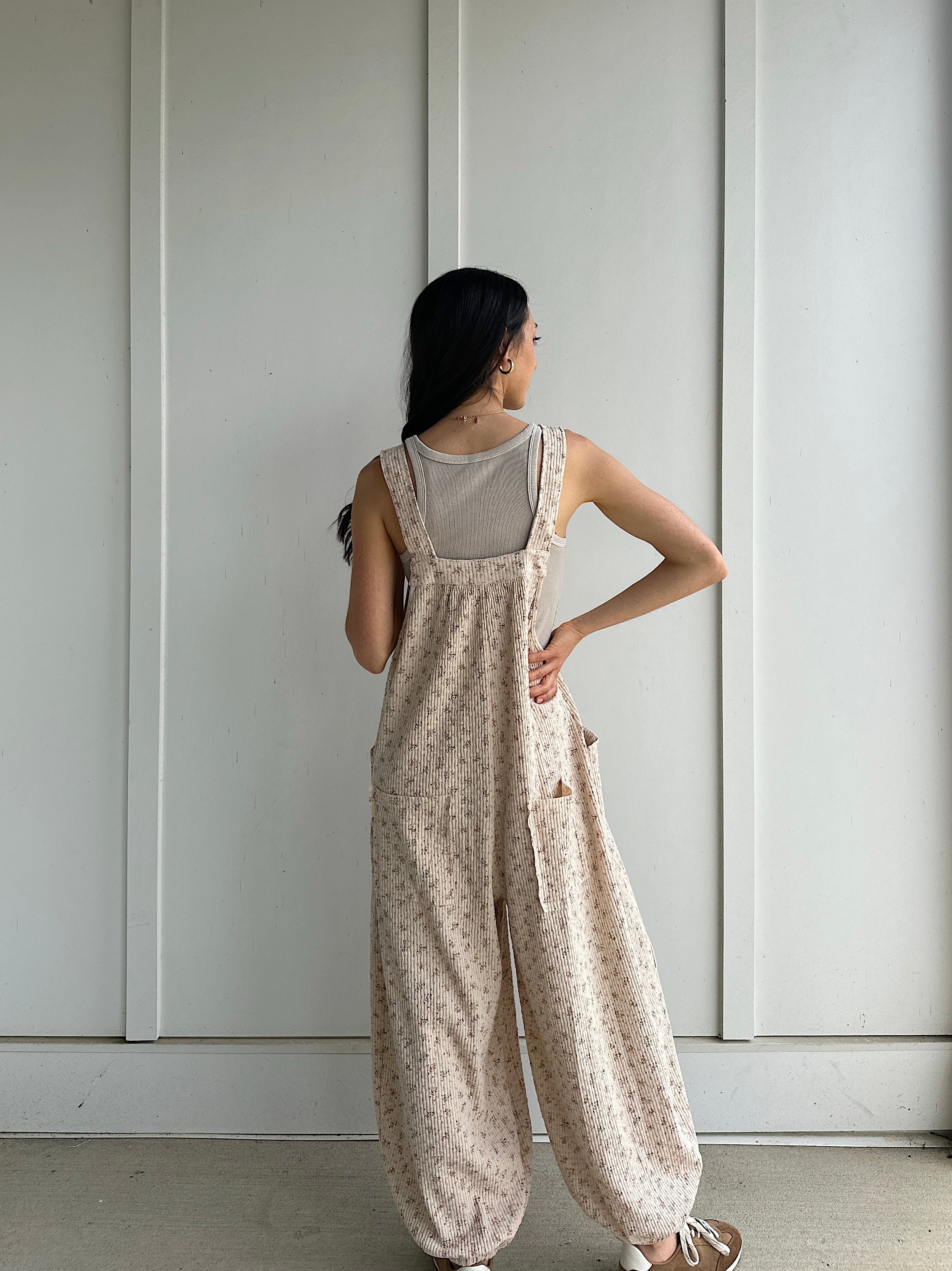 Woman wearing a floral jumpsuit standing against a plain white wall showing the back