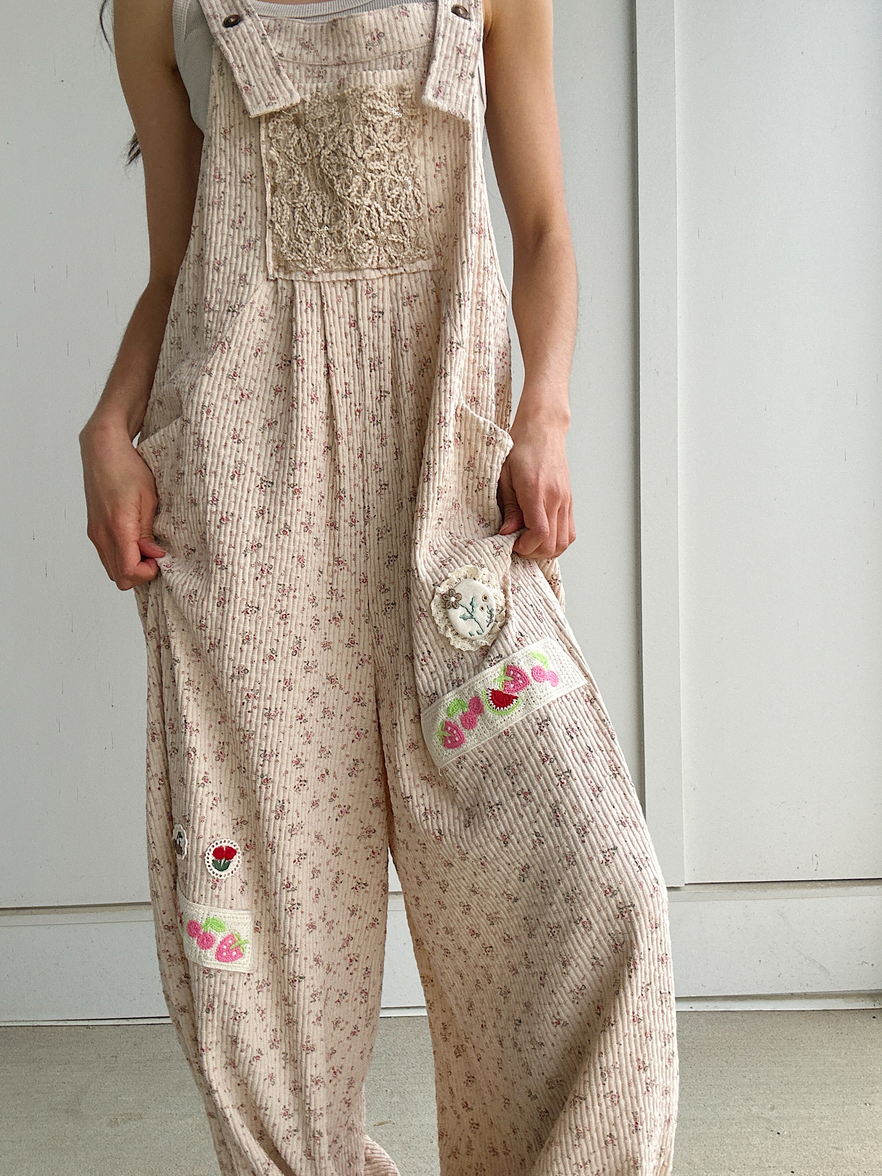 Person wearing beige floral overalls with decorative fruit and flower patches on a plain background