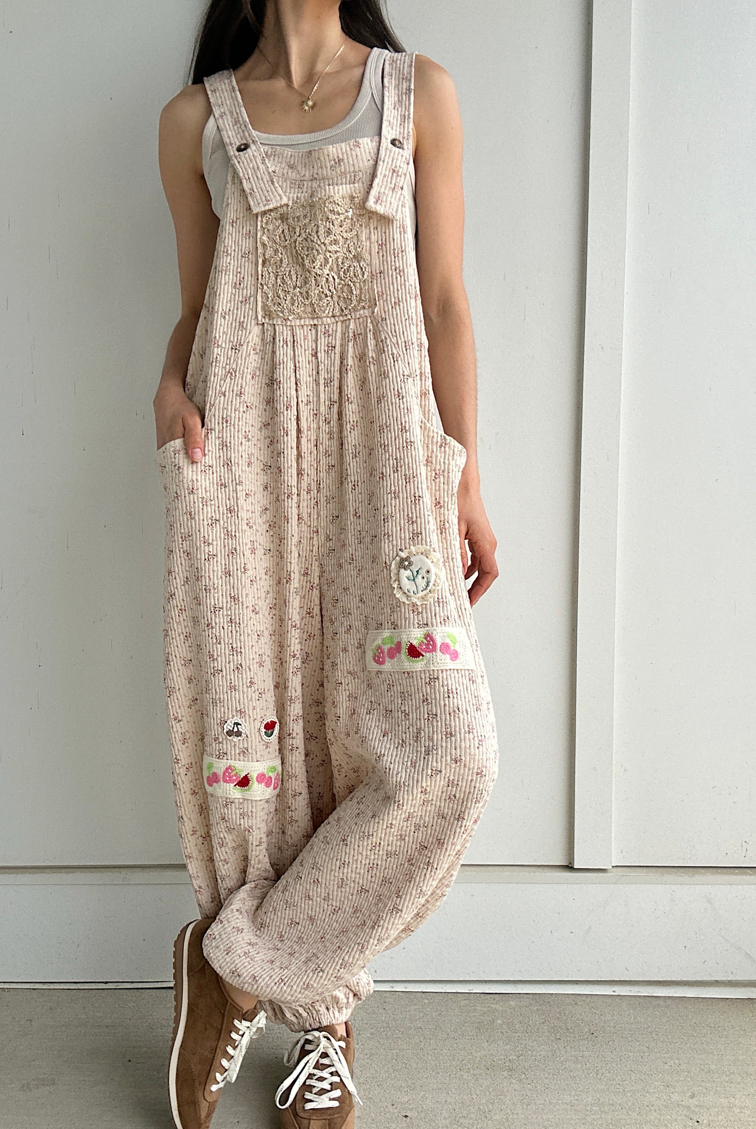 Person wearing a beige floral overalls with a plain background