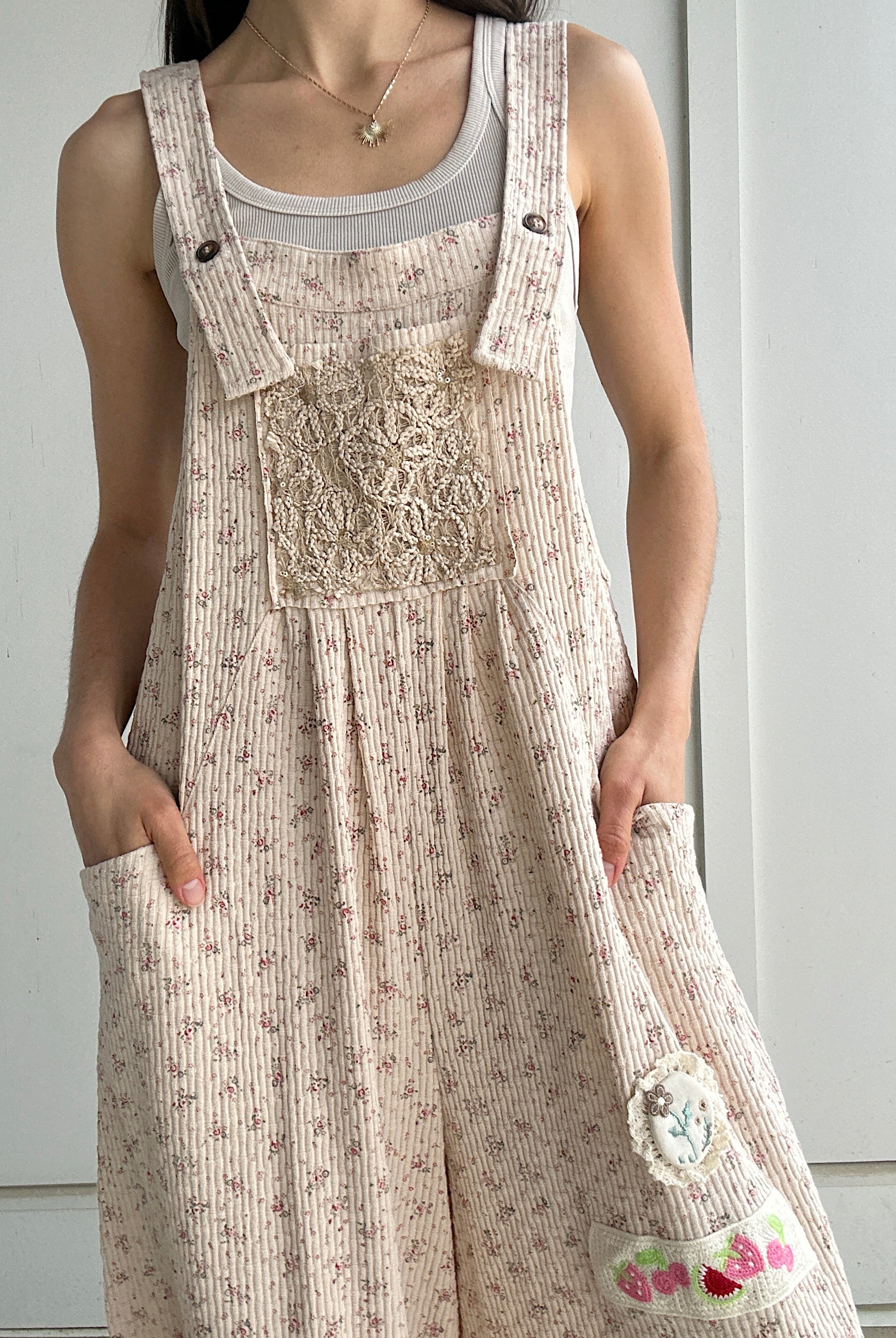 Person wearing a floral overalls with a plain background showing sequin detail on the front patch pocket