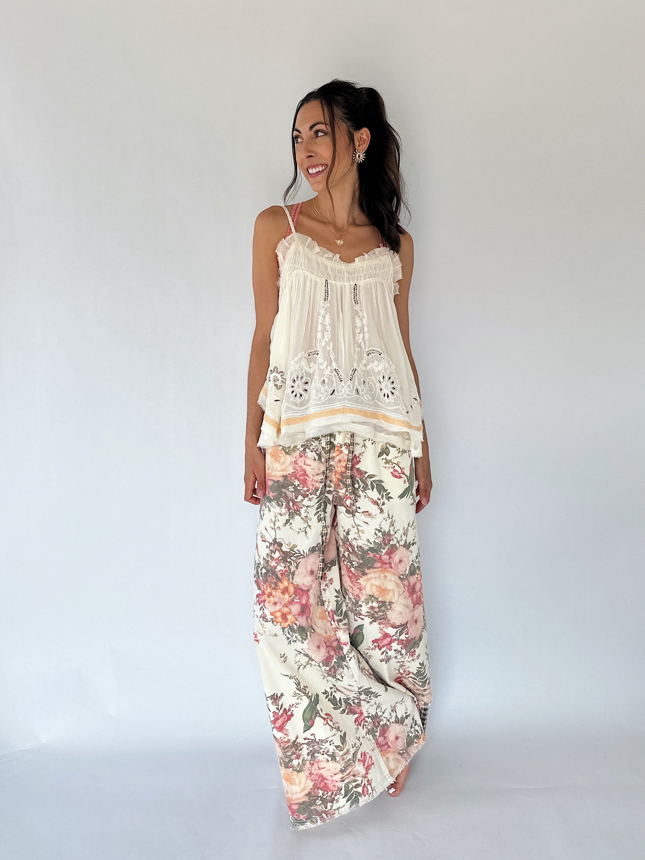 A woman modeling a bohemian-style two-piece outfit consisting of a cream lace camisole top and floral print wide-leg pants, set against a plain white studio background.