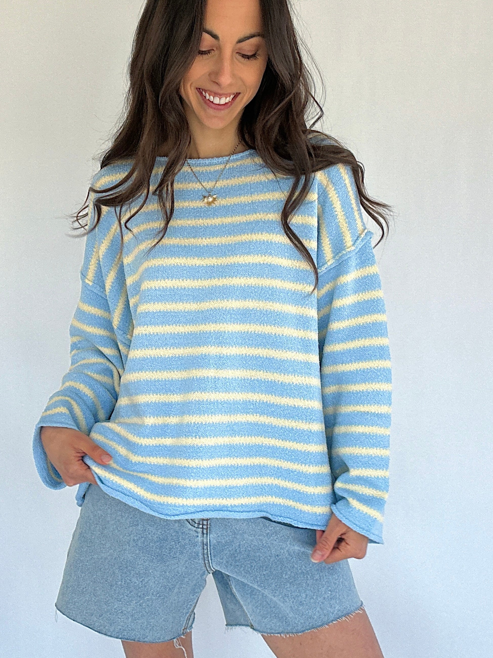 Woman wearing a blue and yellow striped sweater with denim shorts against a white background