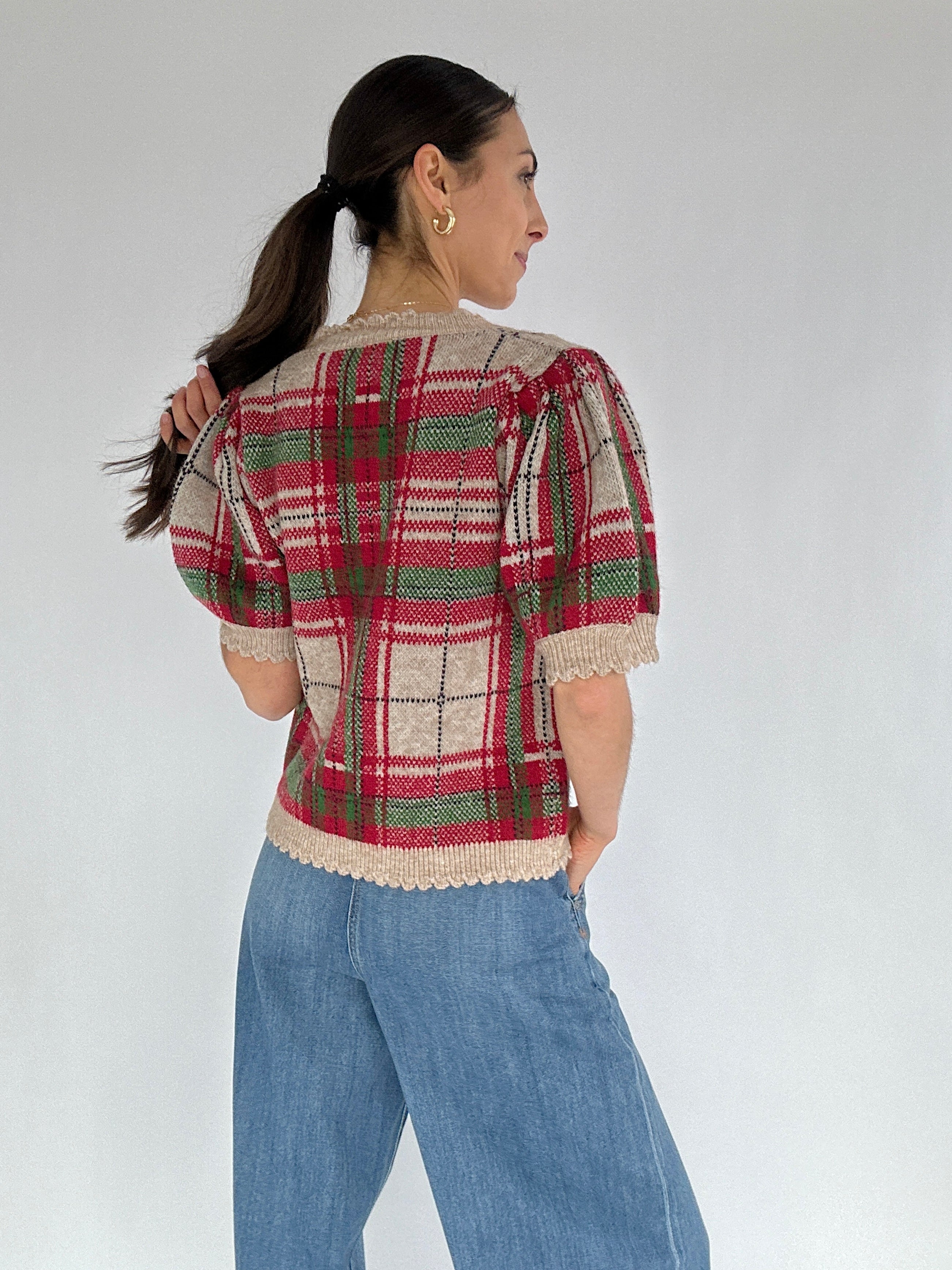 Woman wearing a plaid short sleeve sweater and jeans against a plain background back view
