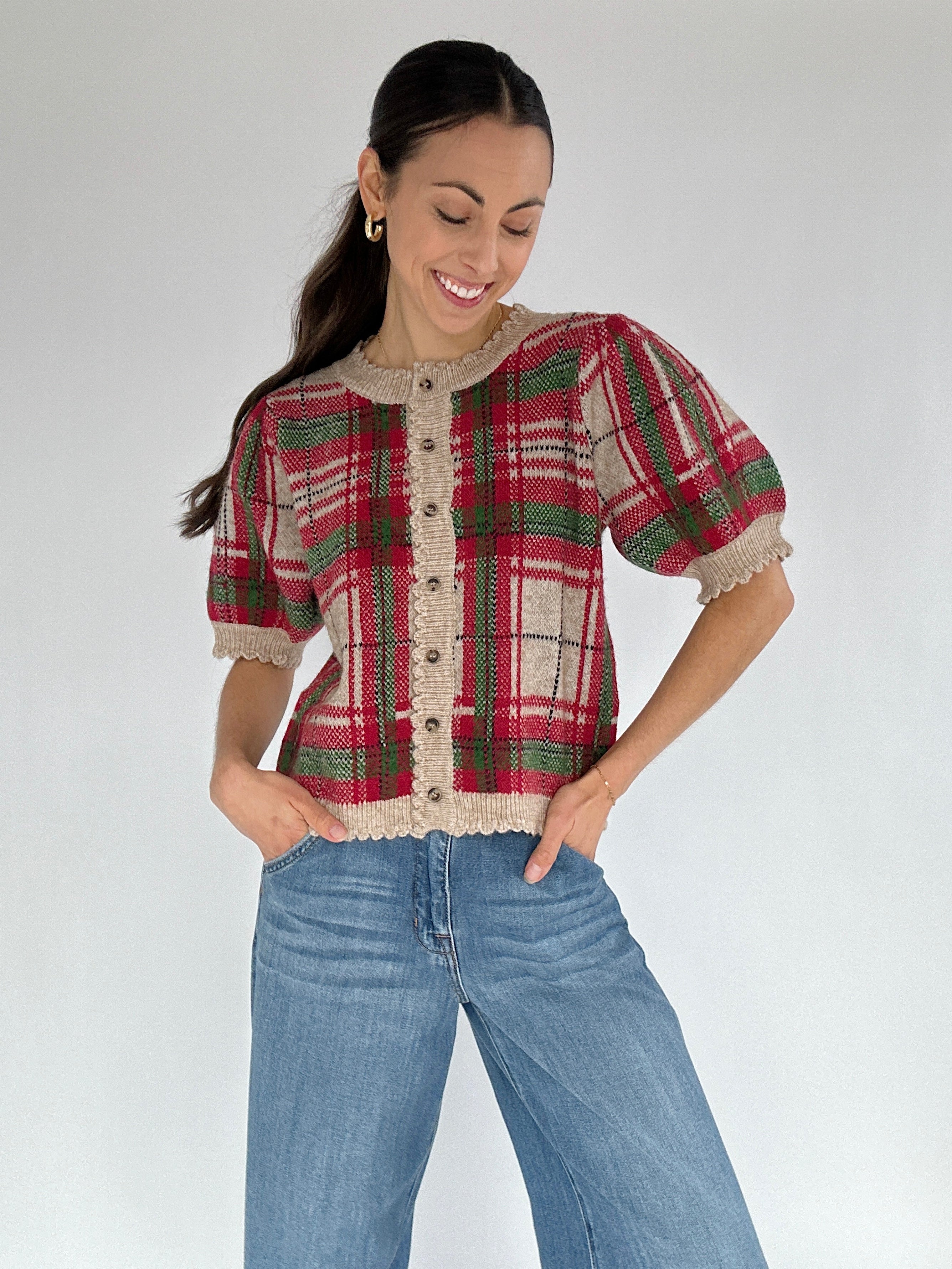 Woman wearing a plaid puff sleeve cardigan top with scalloped edges and jeans on a white background