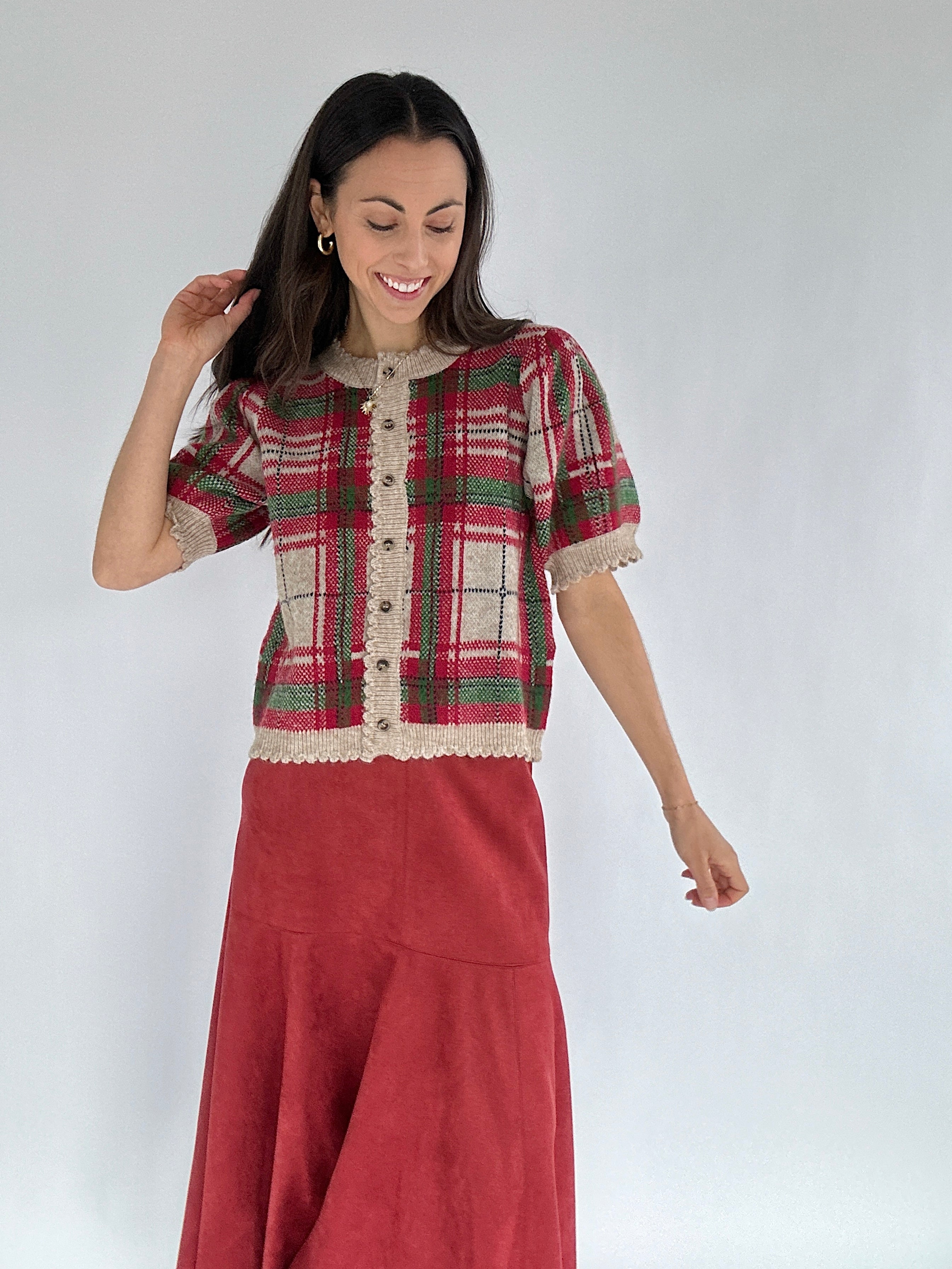 Woman wearing a red plaid sweater top and red skirt against a white background