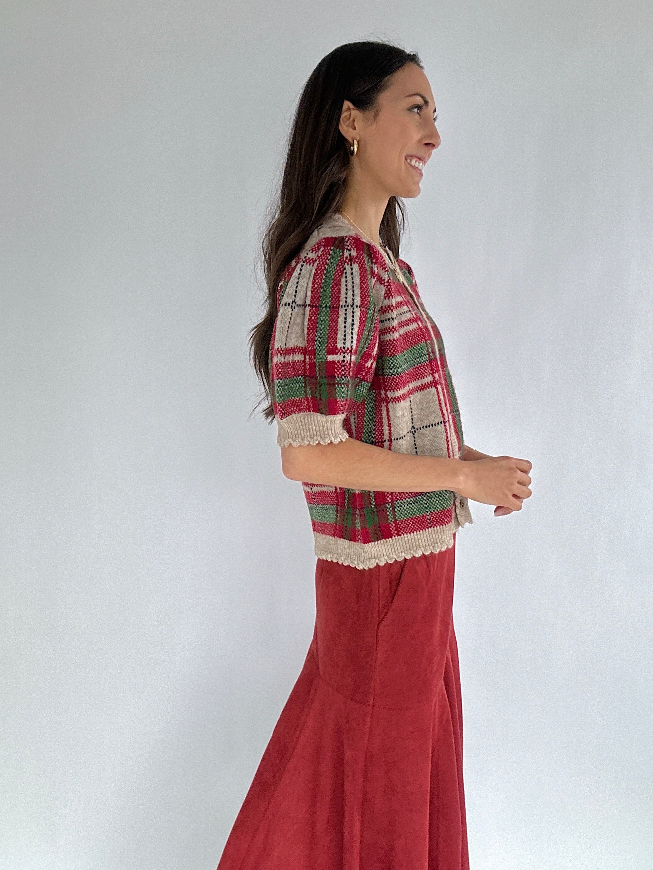 Woman wearing a plaid sweater top and red skirt against a white background from side