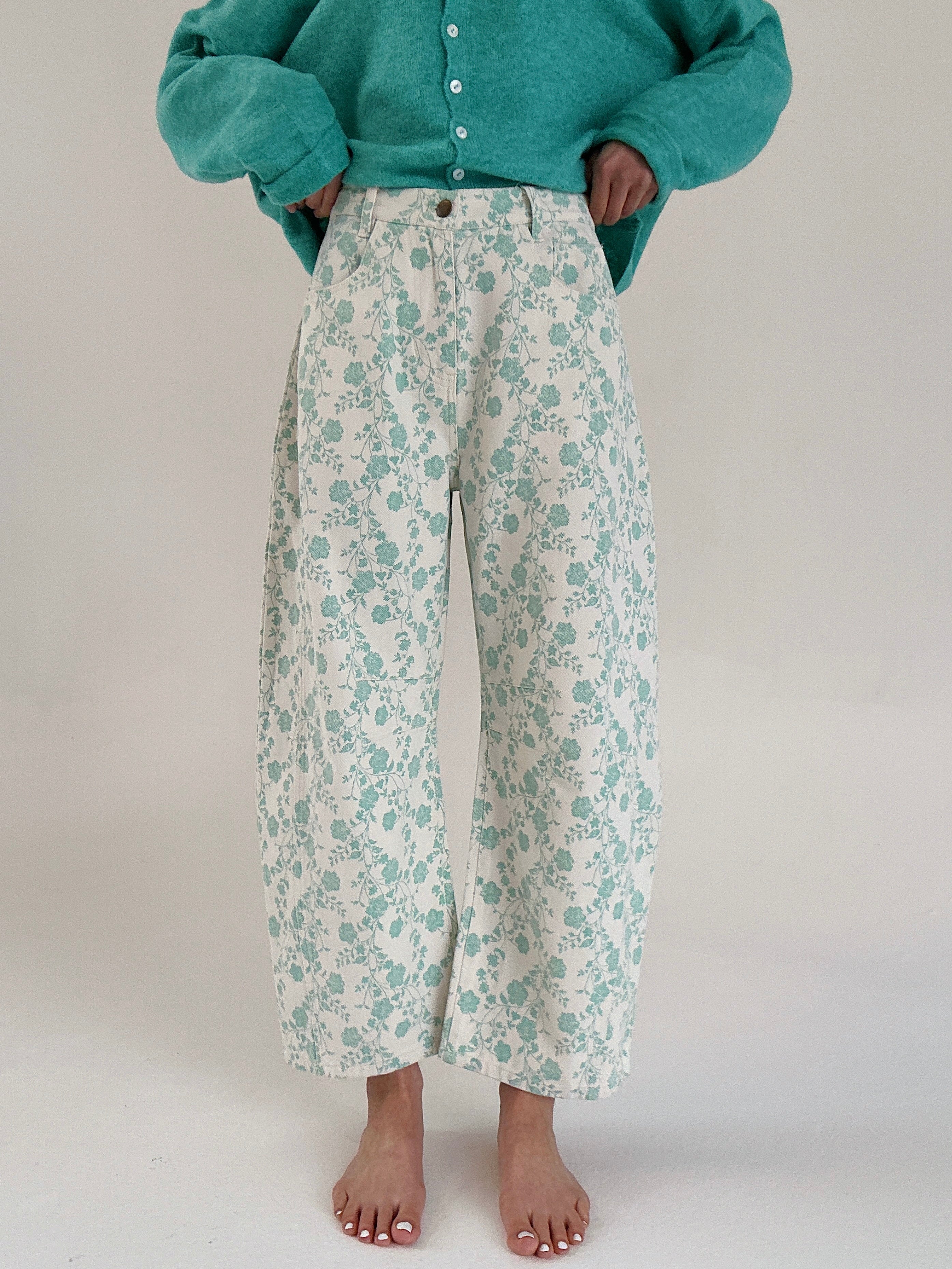 Person wearing floral pants and a teal sweater on a plain background
