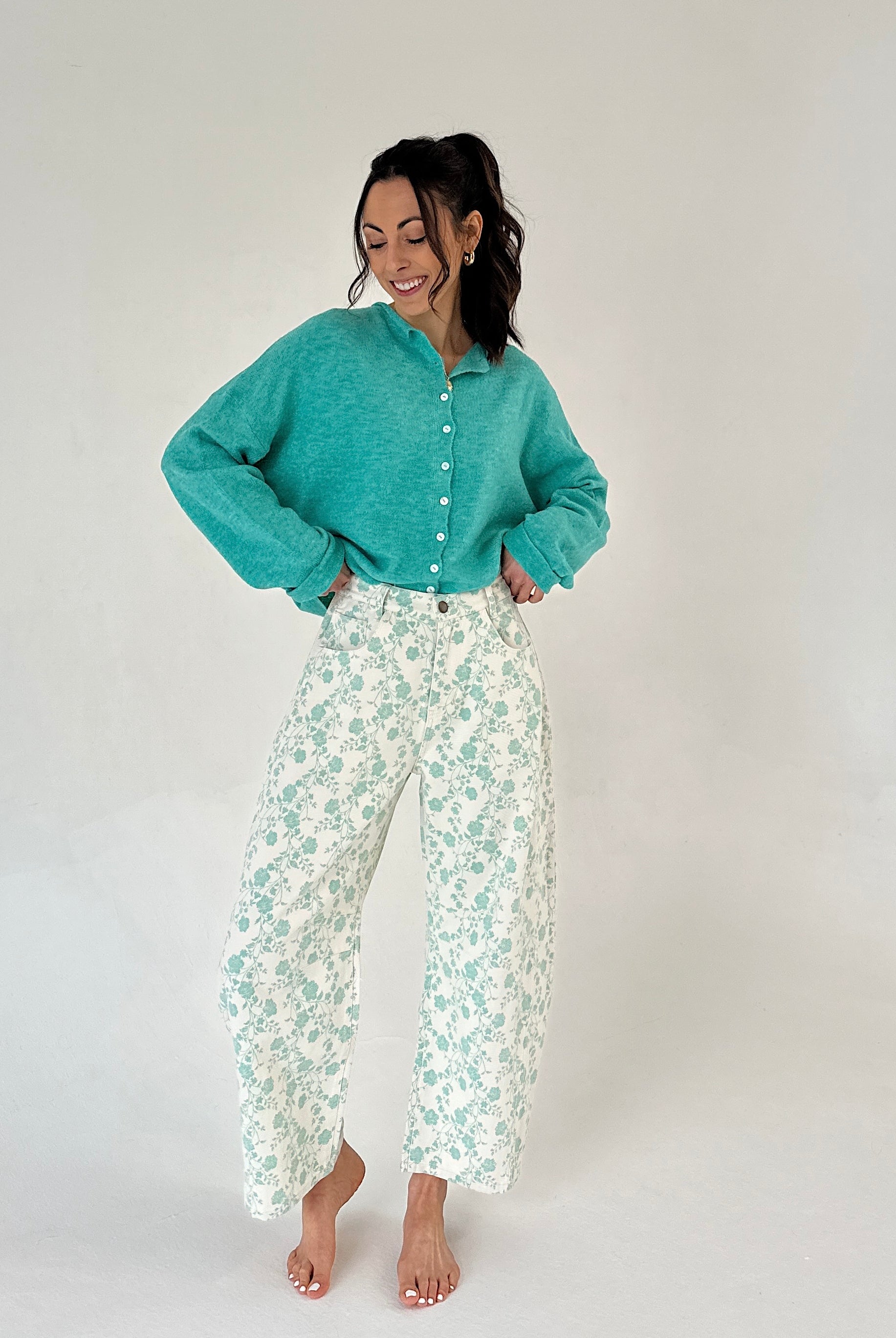 Woman wearing a teal sweater and floral pants on a white background