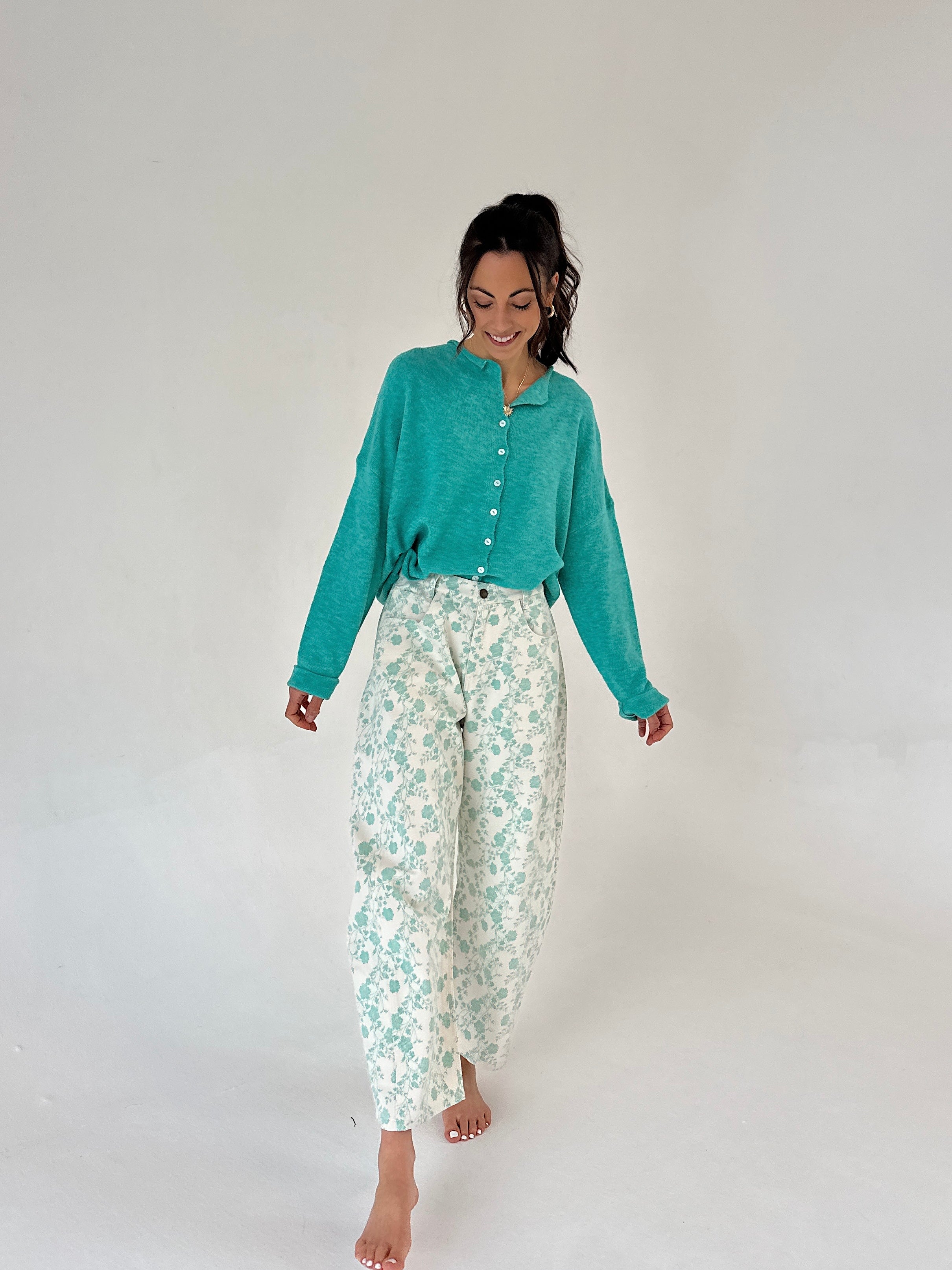 Woman wearing a teal cardigan and floral pants on a white background
