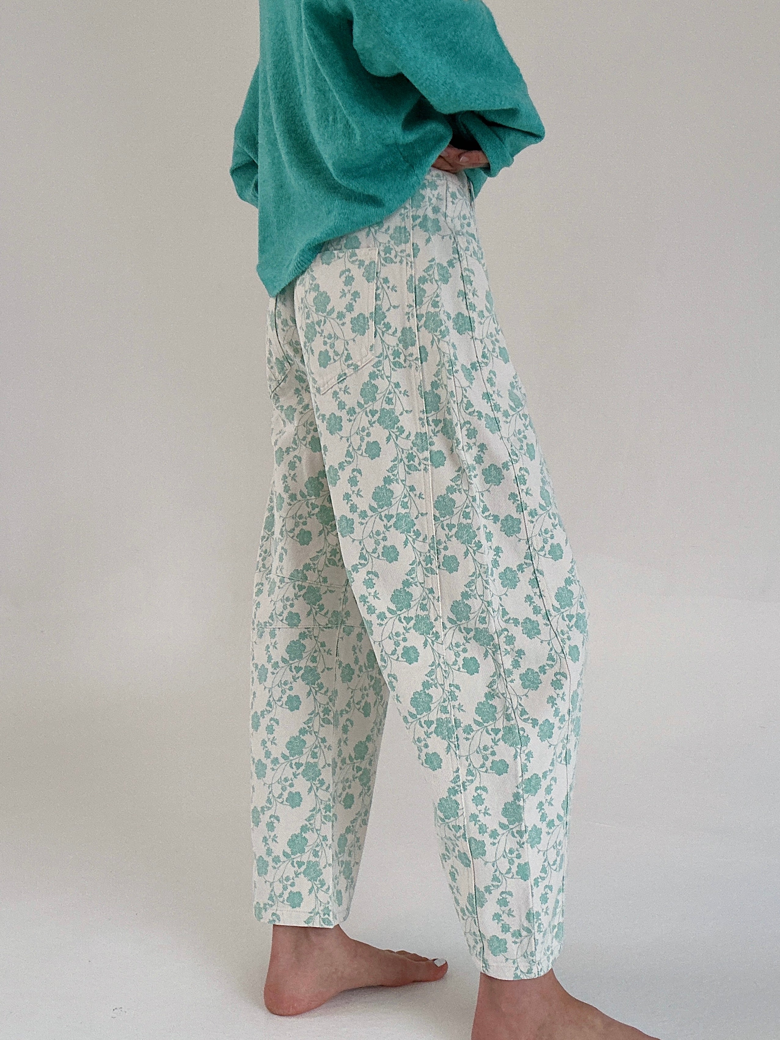 Person wearing teal floral pants and a green sweater on a plain background from side