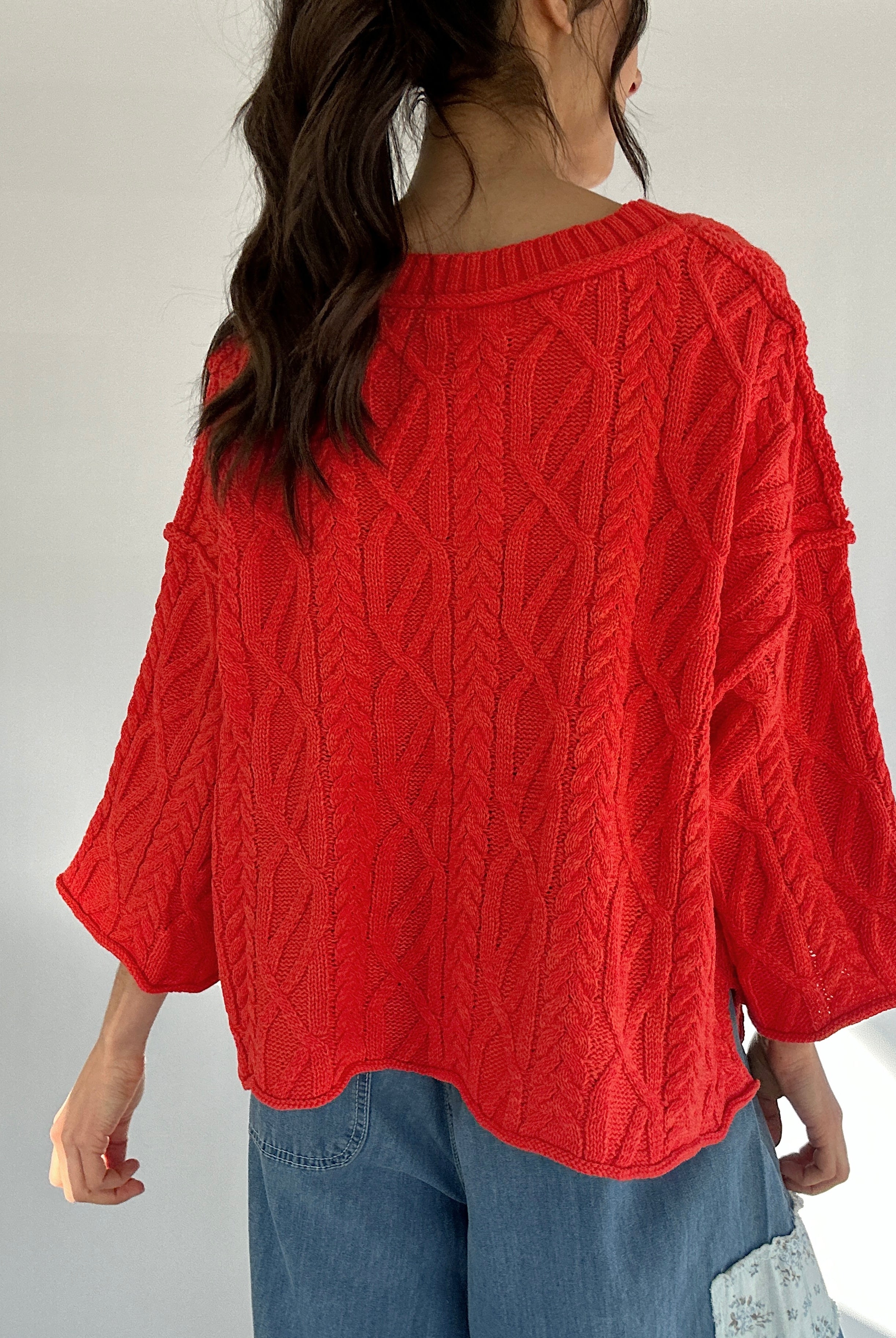 Person wearing a bright coral cable knit sweater with a plain background showing the back