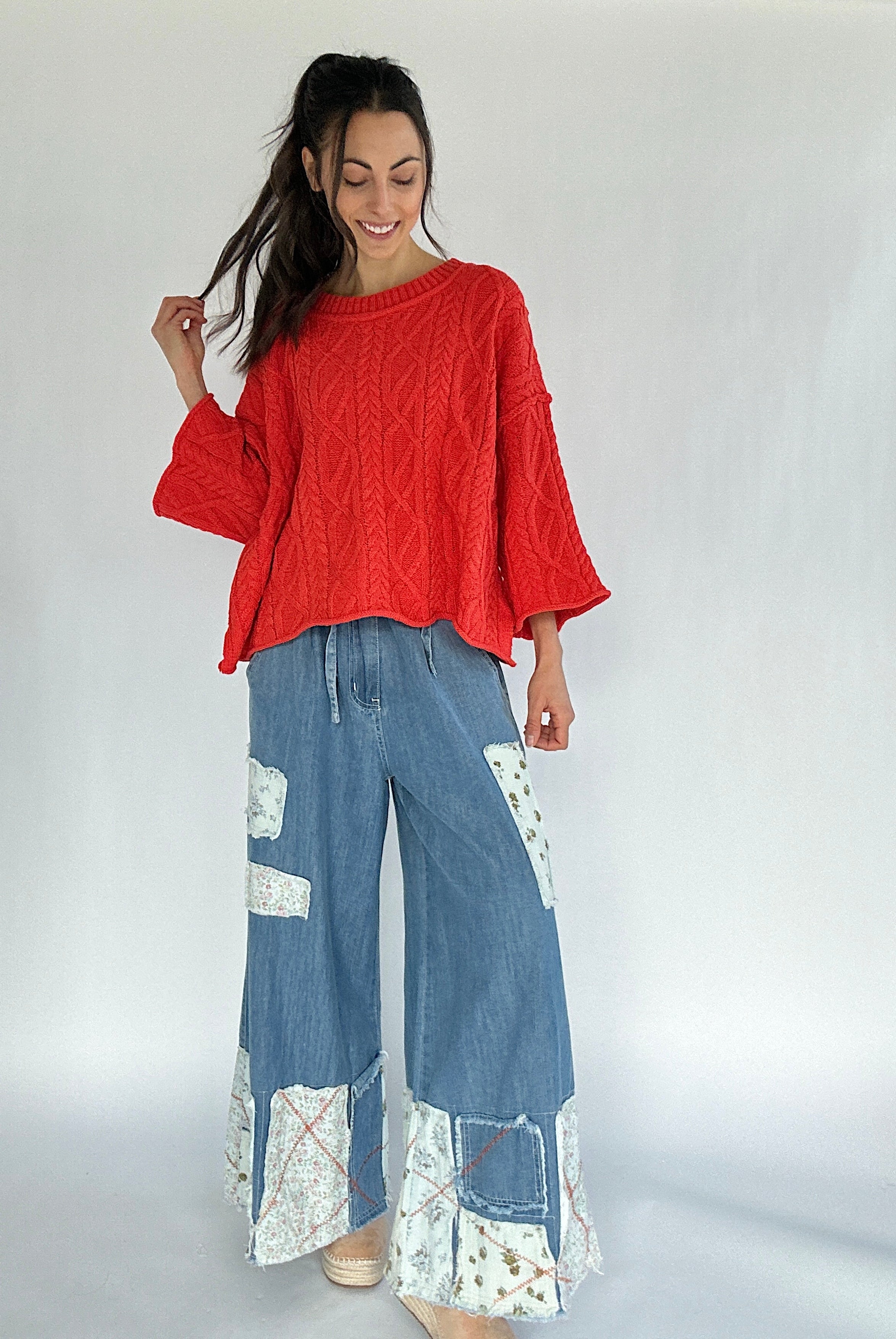 Woman wearing a bright coral sweater and blue patchwork pants on a white background