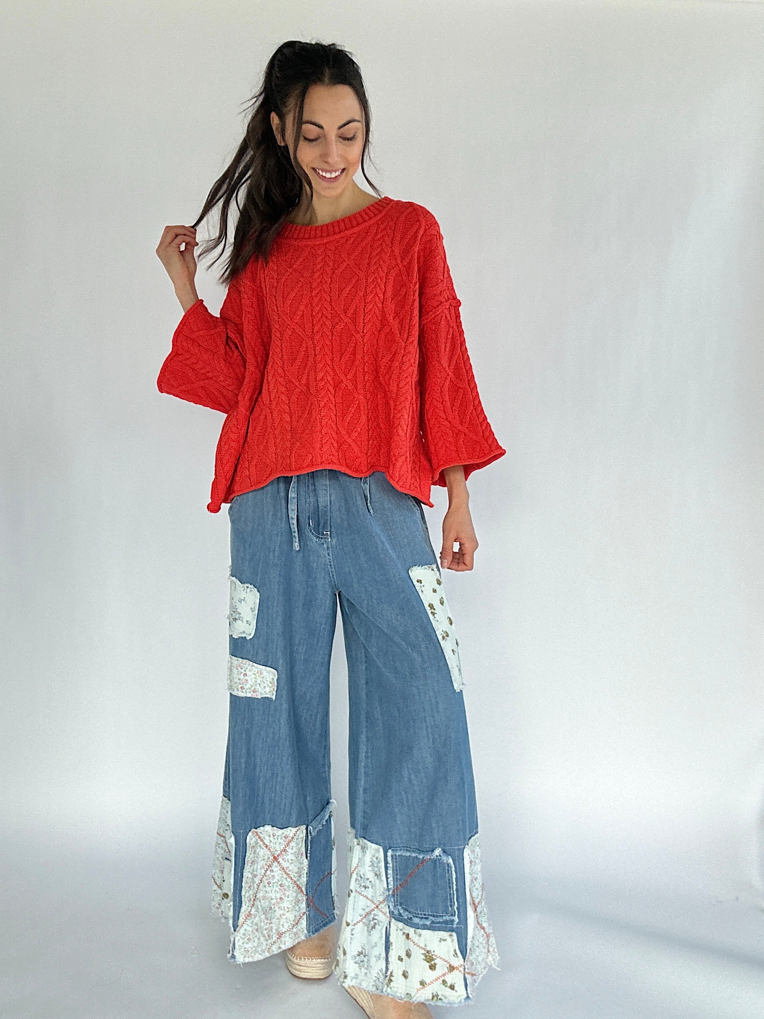 Woman wearing a bright coral sweater and blue patchwork pants on a white background