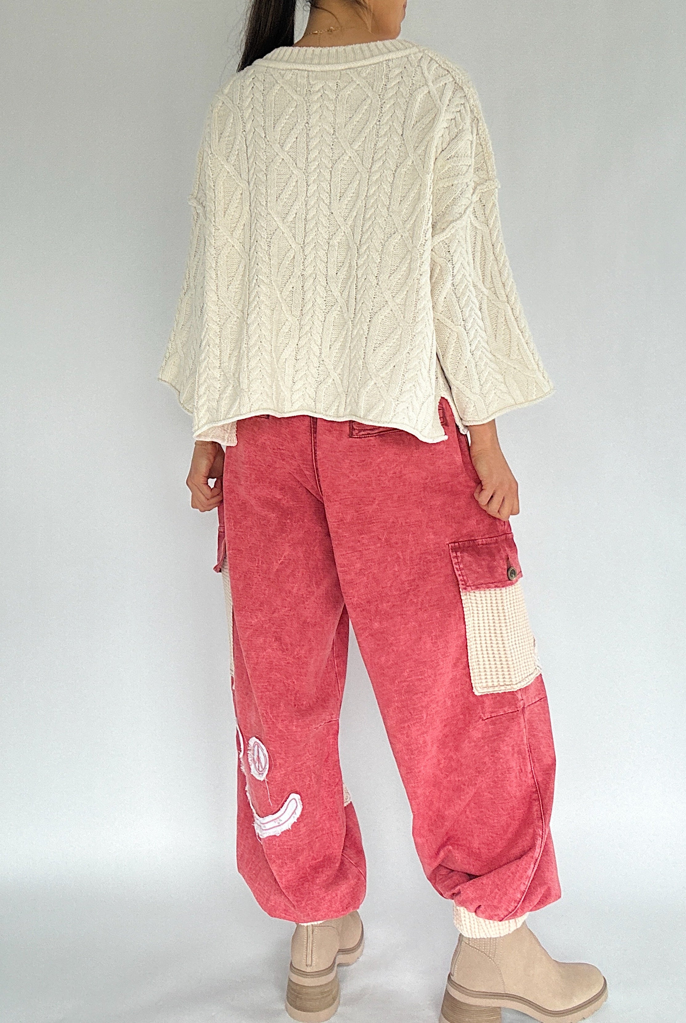 Person wearing a cream sweater and red cargo pants on a plain background back view