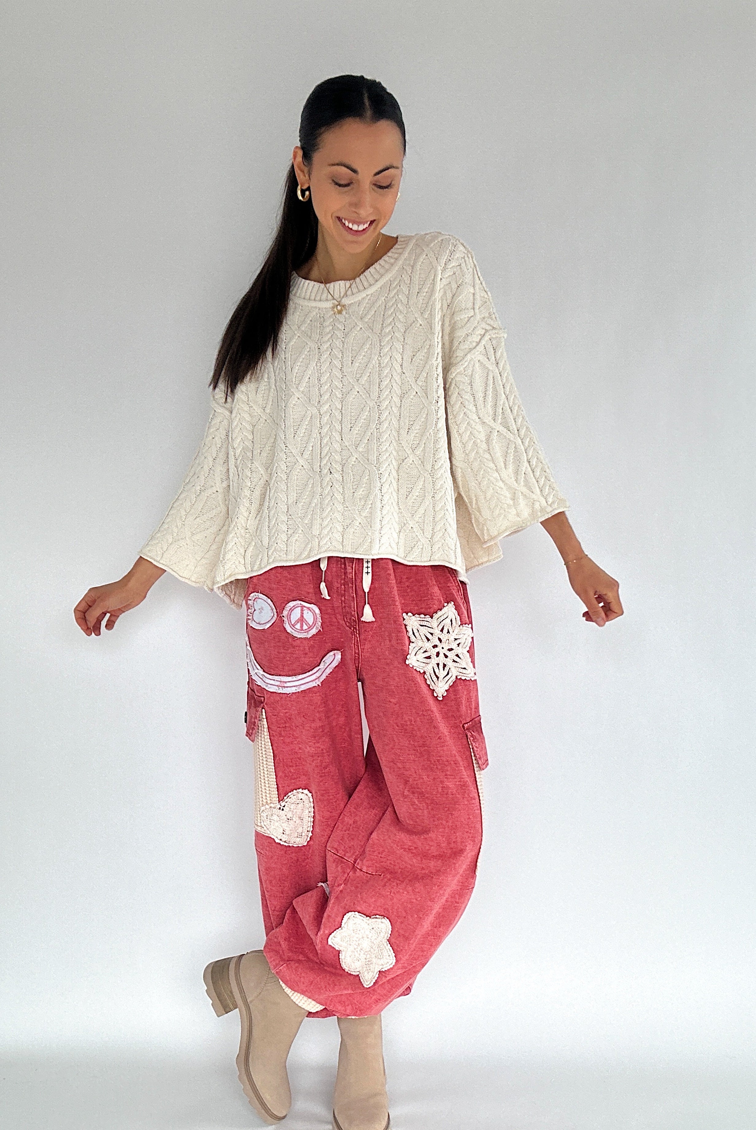 Woman wearing a cream sweater and red pants with patchwork patterns on a plain background