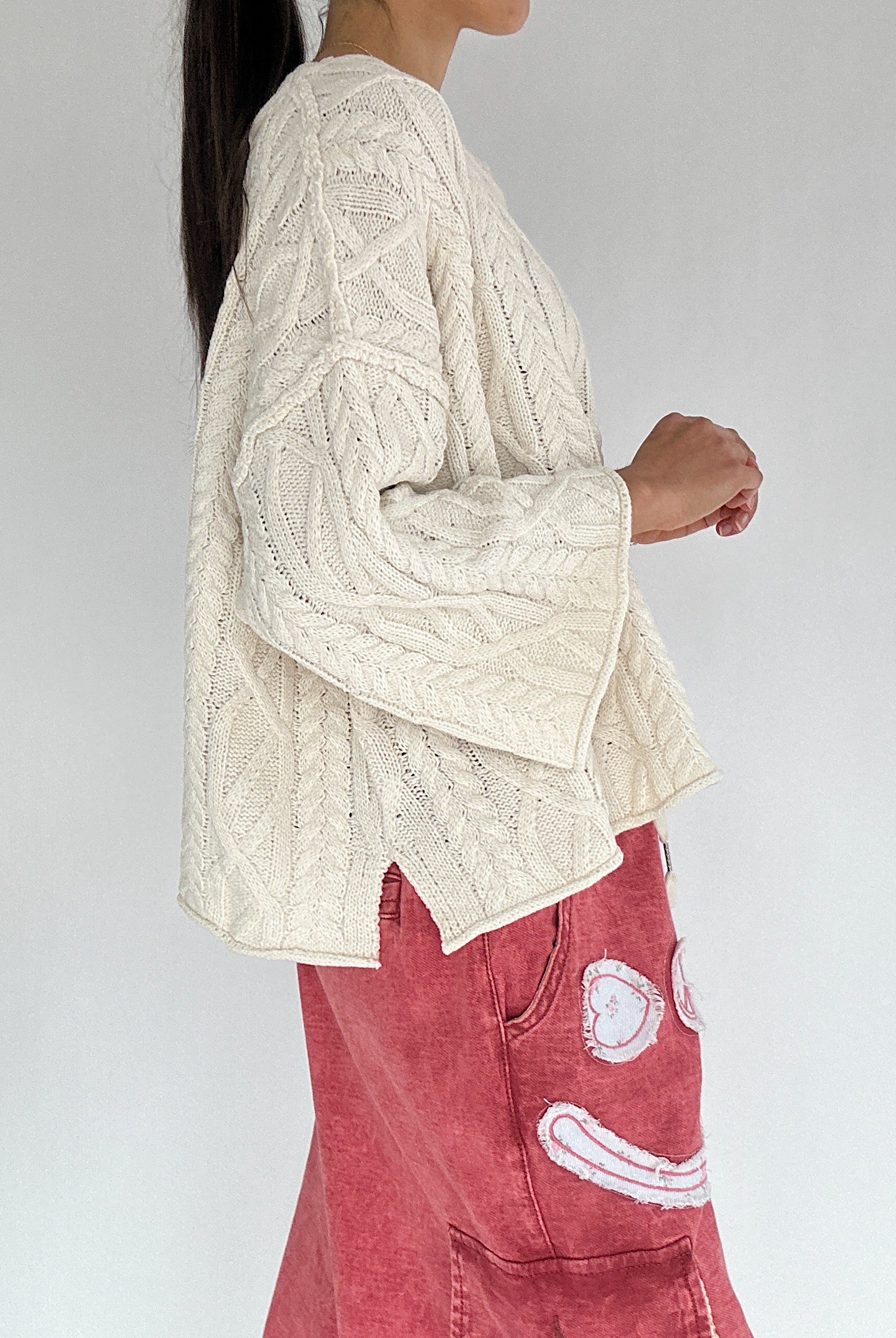 Person wearing a cream cable knit sweater and red pants with a white background