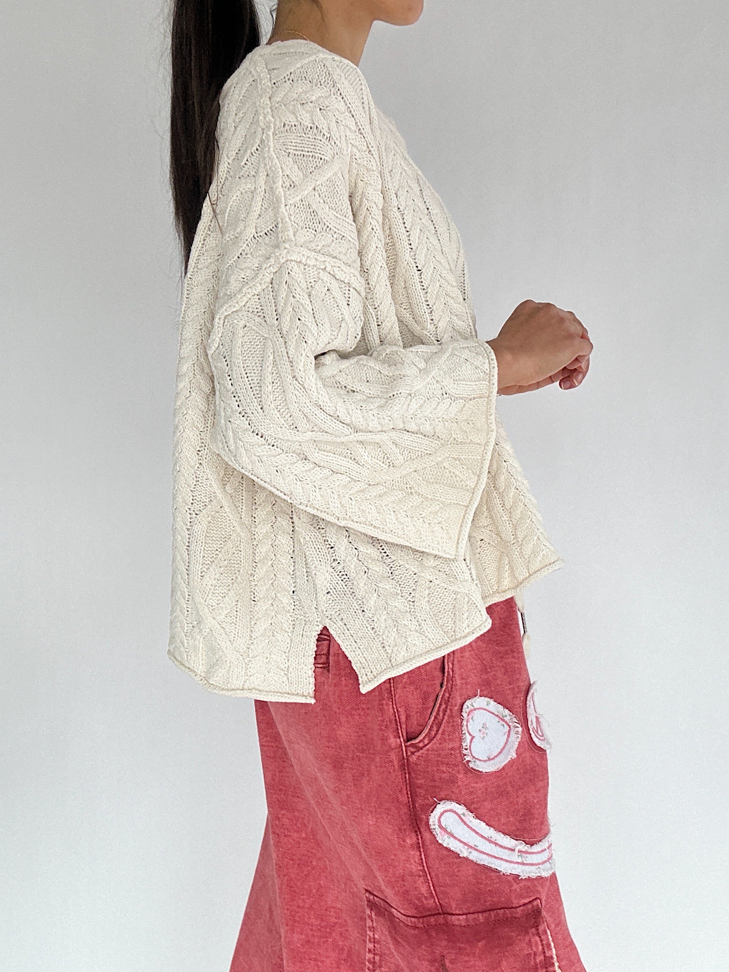 Person wearing a cream cable knit sweater and red pants with a white background