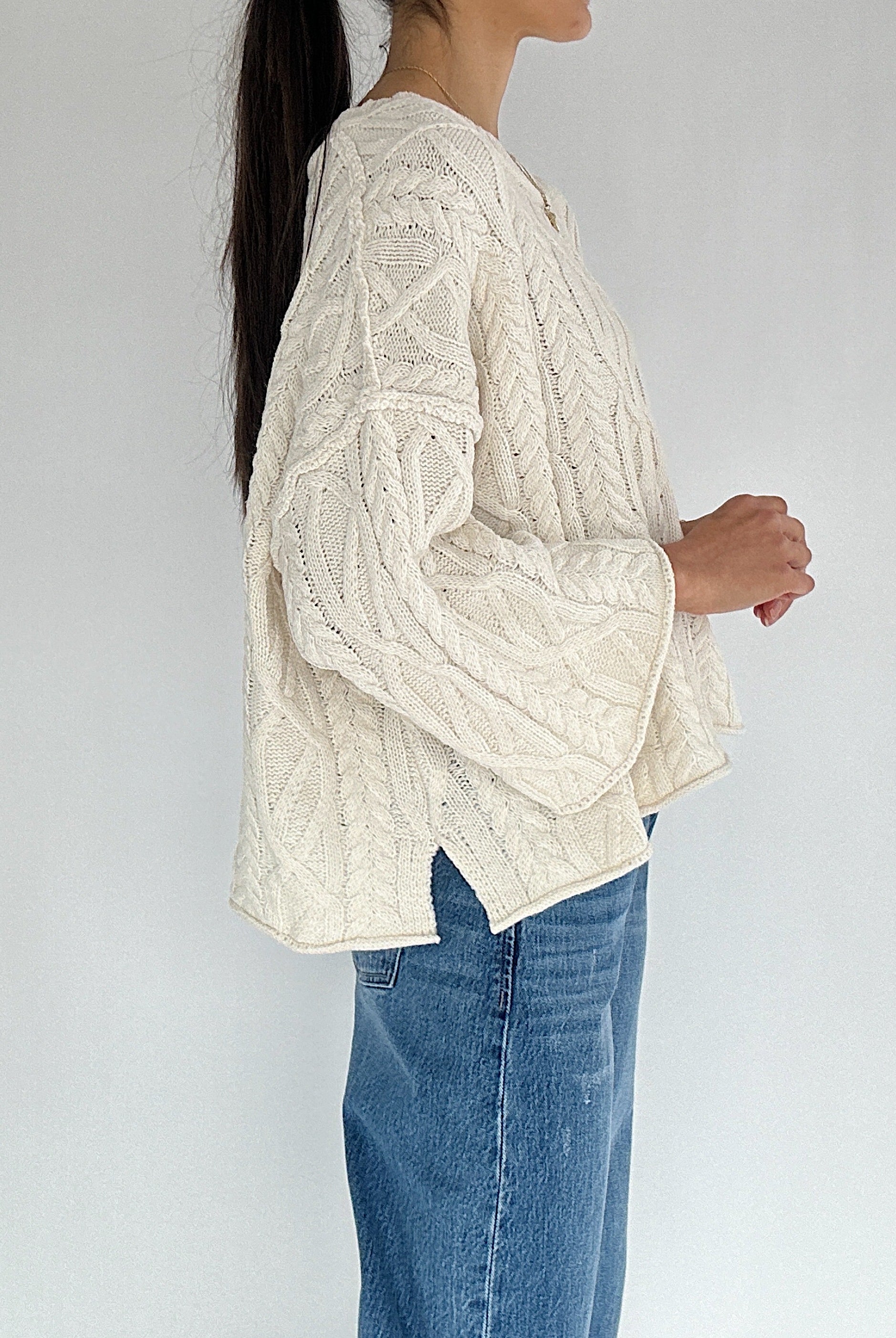 Person wearing a cream cable knit sweater and blue jeans against a white background