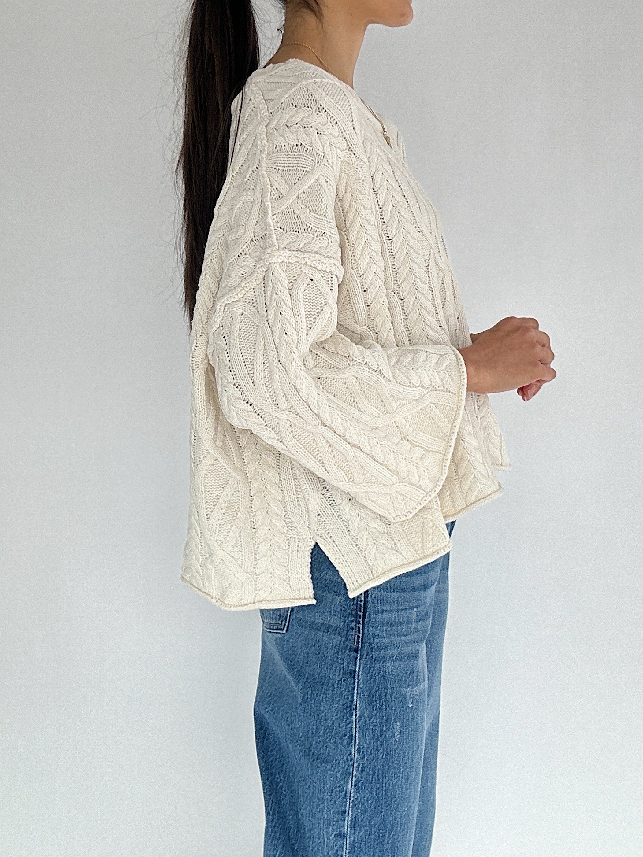 Person wearing a cream cable knit sweater and blue jeans against a white background
